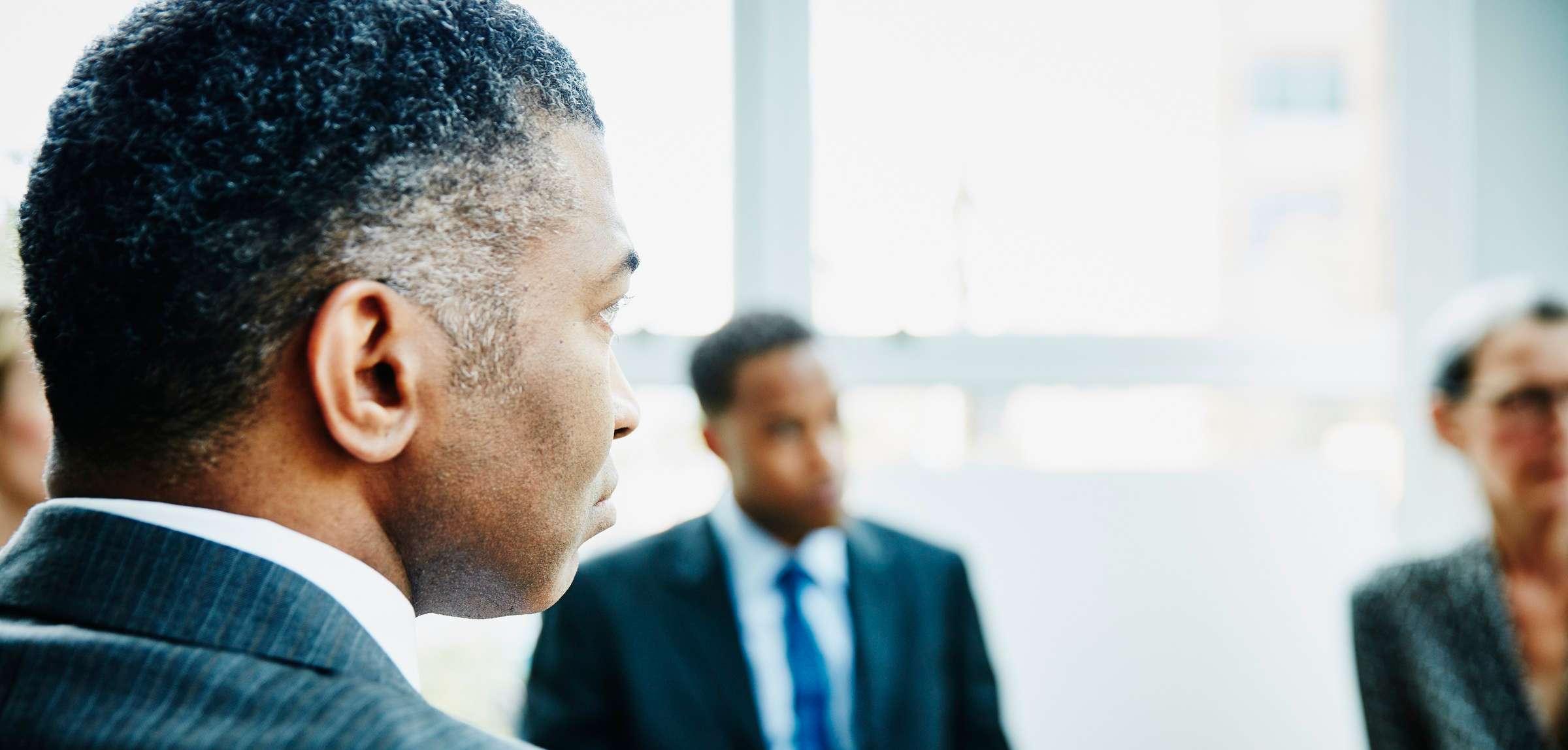 Allianz Gesundheitswelt - Informationen für Arbeitgeber: Ein dunkelhäutiger Mann im Anzug sitzt mit dem Rücken zur Kamera