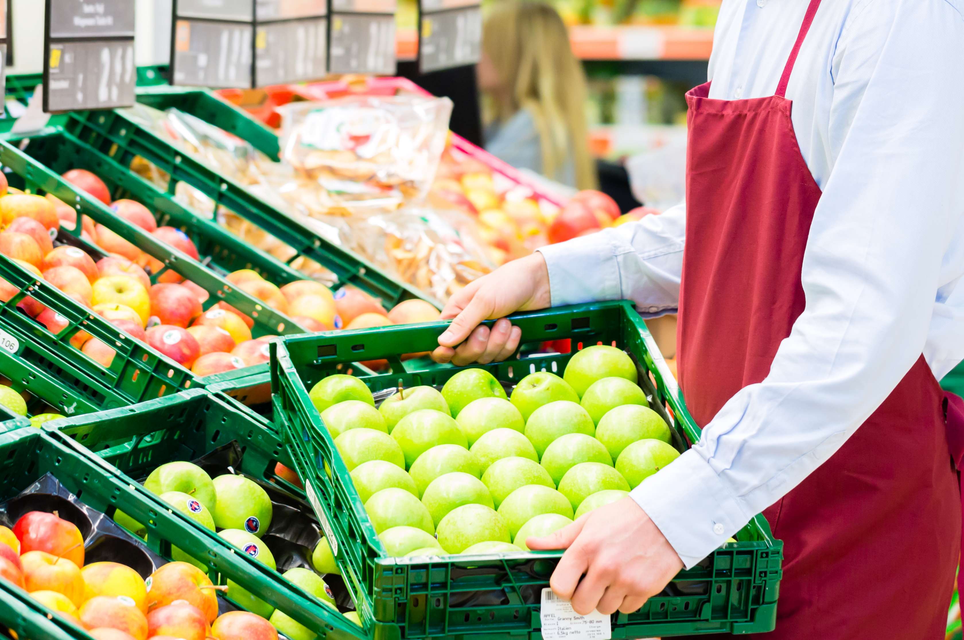 Allianz Gesundheitswelt - Check Arbeitspositionen im Alltag: Ein Einhandelskaufmann verräumt eine Kiste Äpfel im Supermarkt.