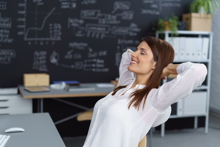 Allianz Gesundheitswelt - Check Sitzpositionen im Büro: eine junge Frau mit langen braunen Haaren und weißer Bluse streckt sich auf ihrem Bürostühl.