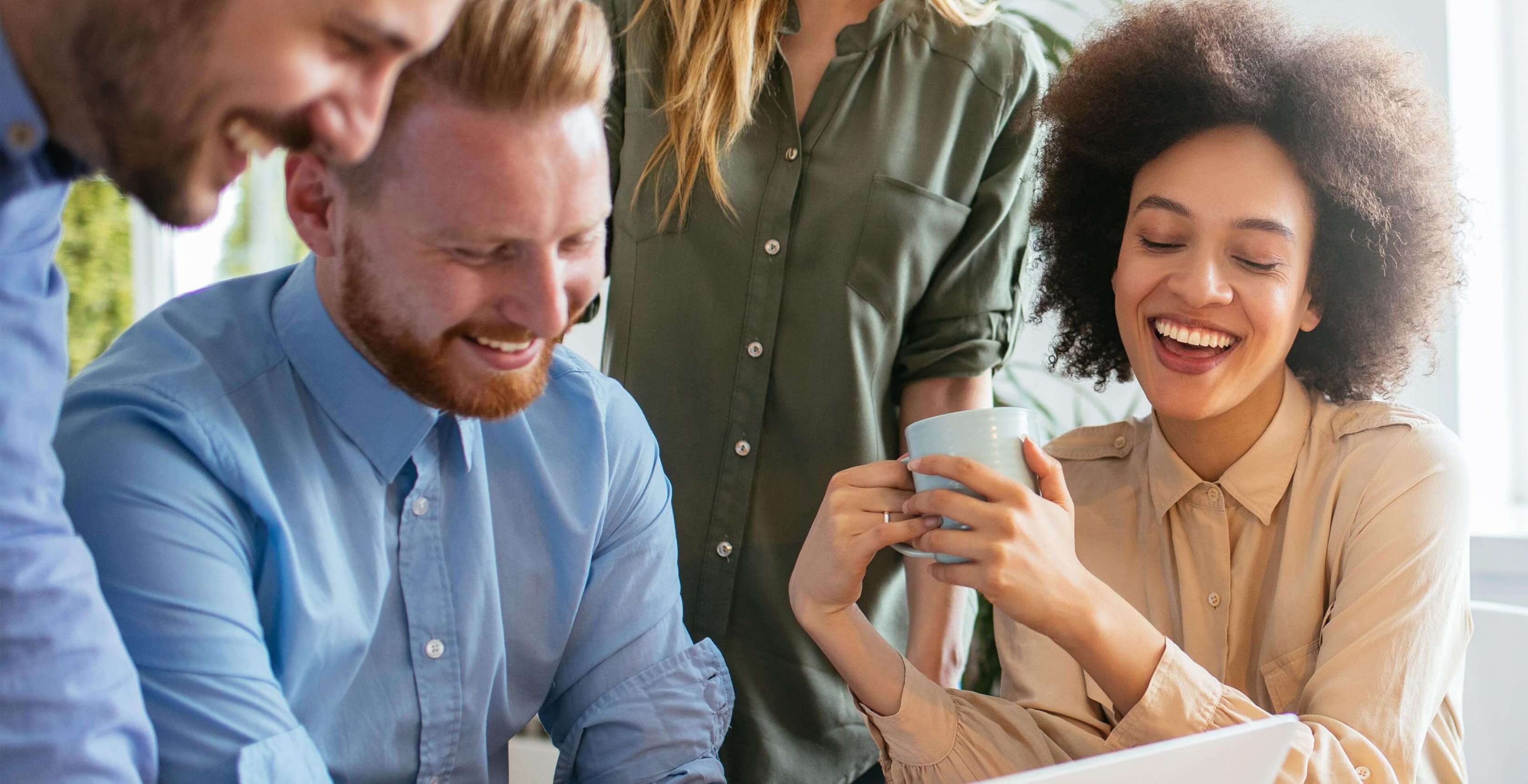 Allianz Gesundheitswelt - Tipps für gesunden Büroalltag: Eine Gruppe von Arbeitskollegen sitzt geseinsam am Tisch und tauscht sich über Informationen am Laptop aus. Die Frau auf der rechten Seite hält eine Kaffeetasse in der Hand.