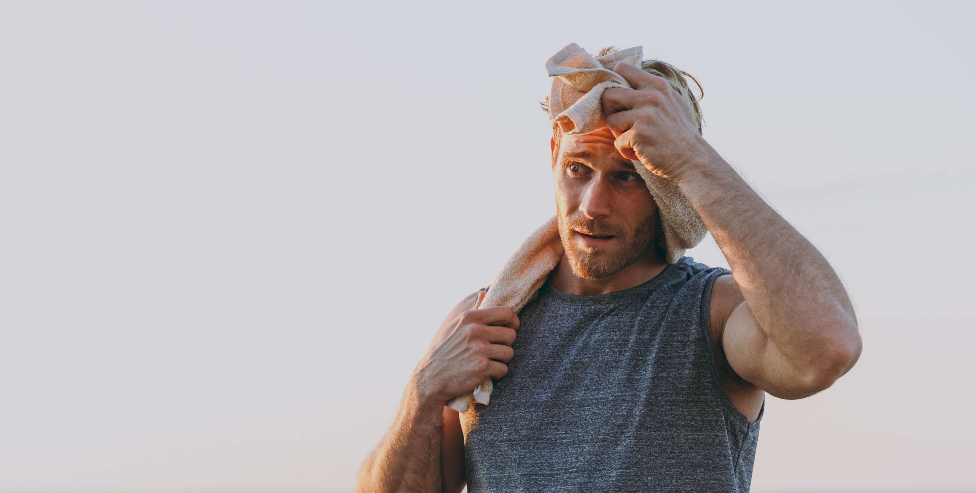 Allianz Gesundheitswelt - Joggen im Alltag: Ein Mann mit grauem Laufshirt wischt sich am Meer mit einem Handtuch den Schweiß von der Stirn.