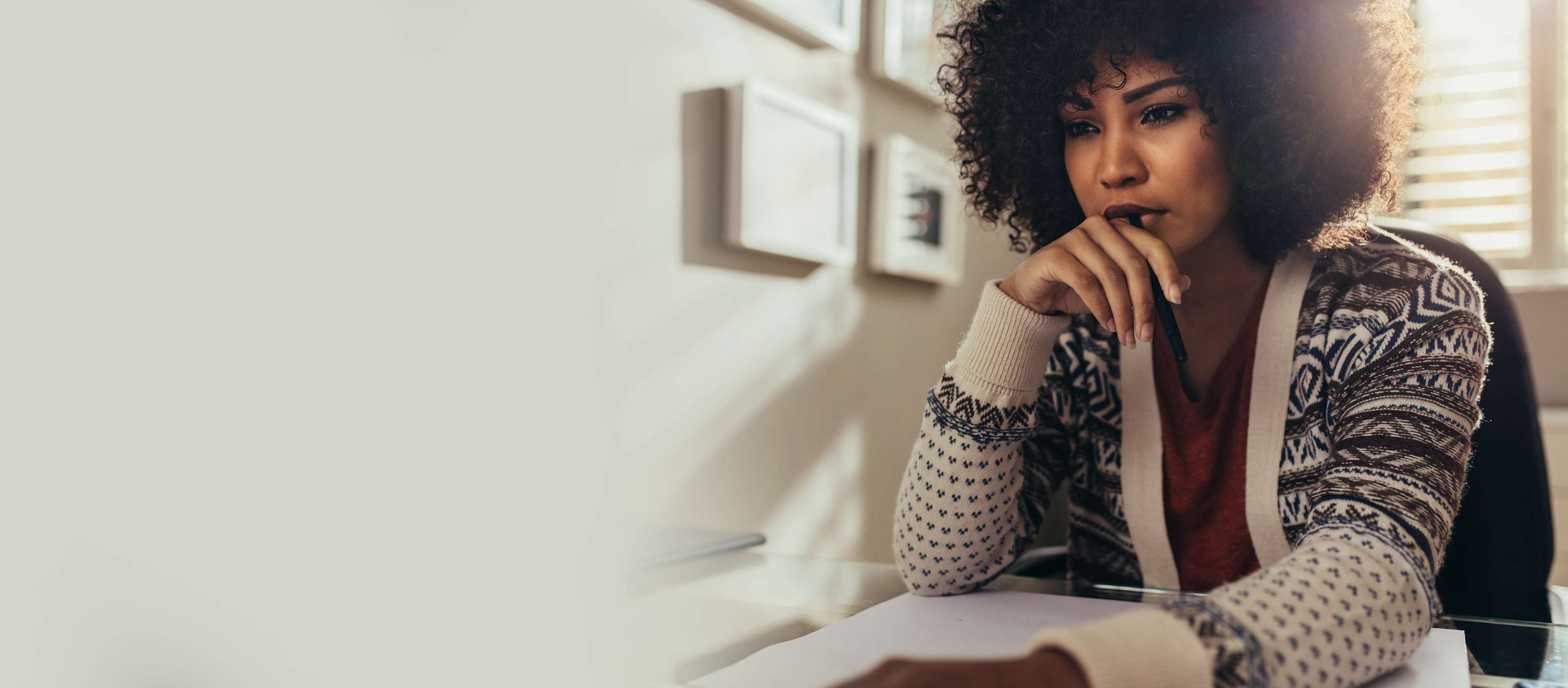 Allianz Gesundheitswelt - Gedächtnis-Check Online: eine Frau mit Locken und gemusterter Strickjacke sitzt nachdenklich an einem Tisch. 