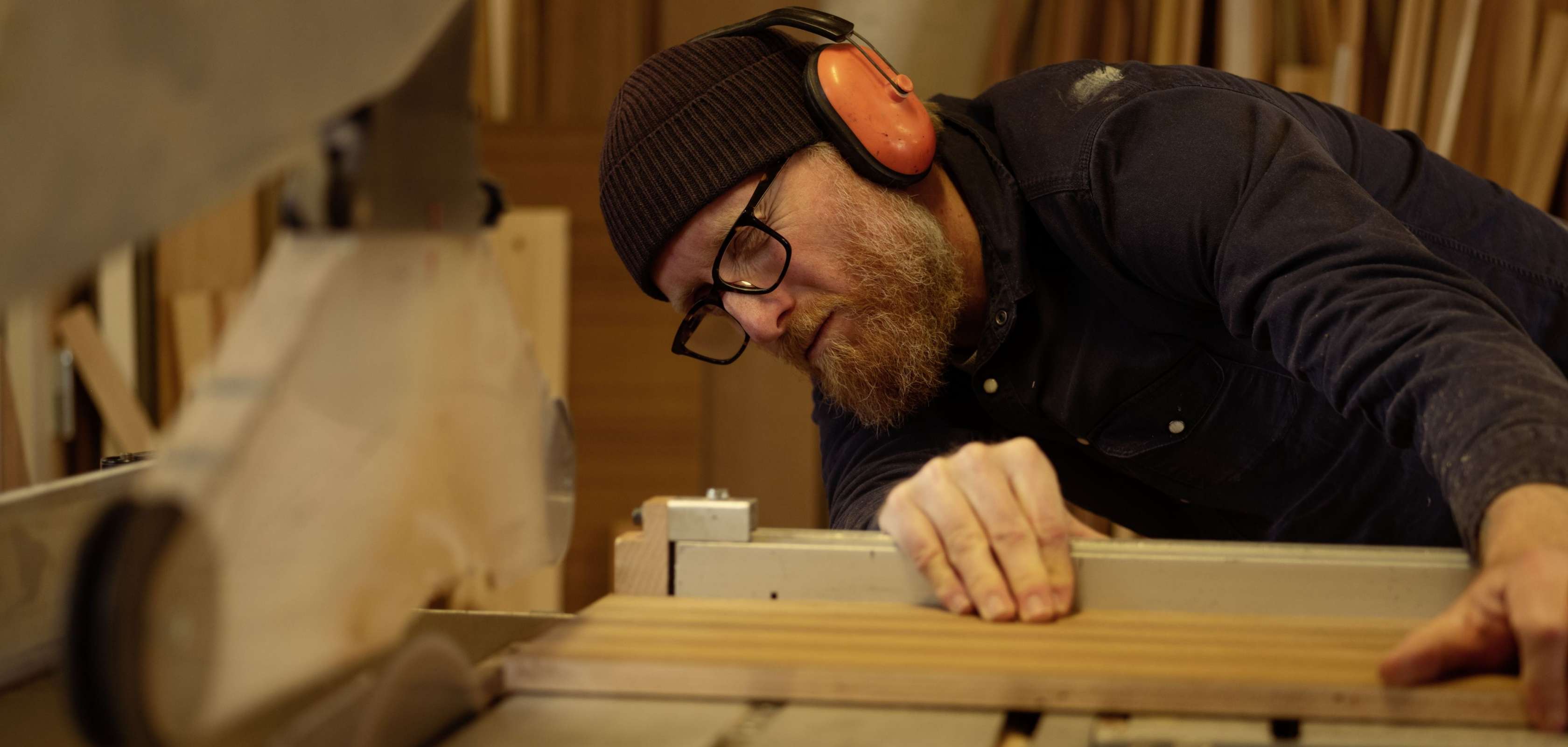 Allianz Gesundheitswelt - Gesundheits-Test: Ein Mann mit schwarzer Mütze und orangenen Ohrenschützern steht in einer Werkstatt und richtet Holz und Metallteile aus.