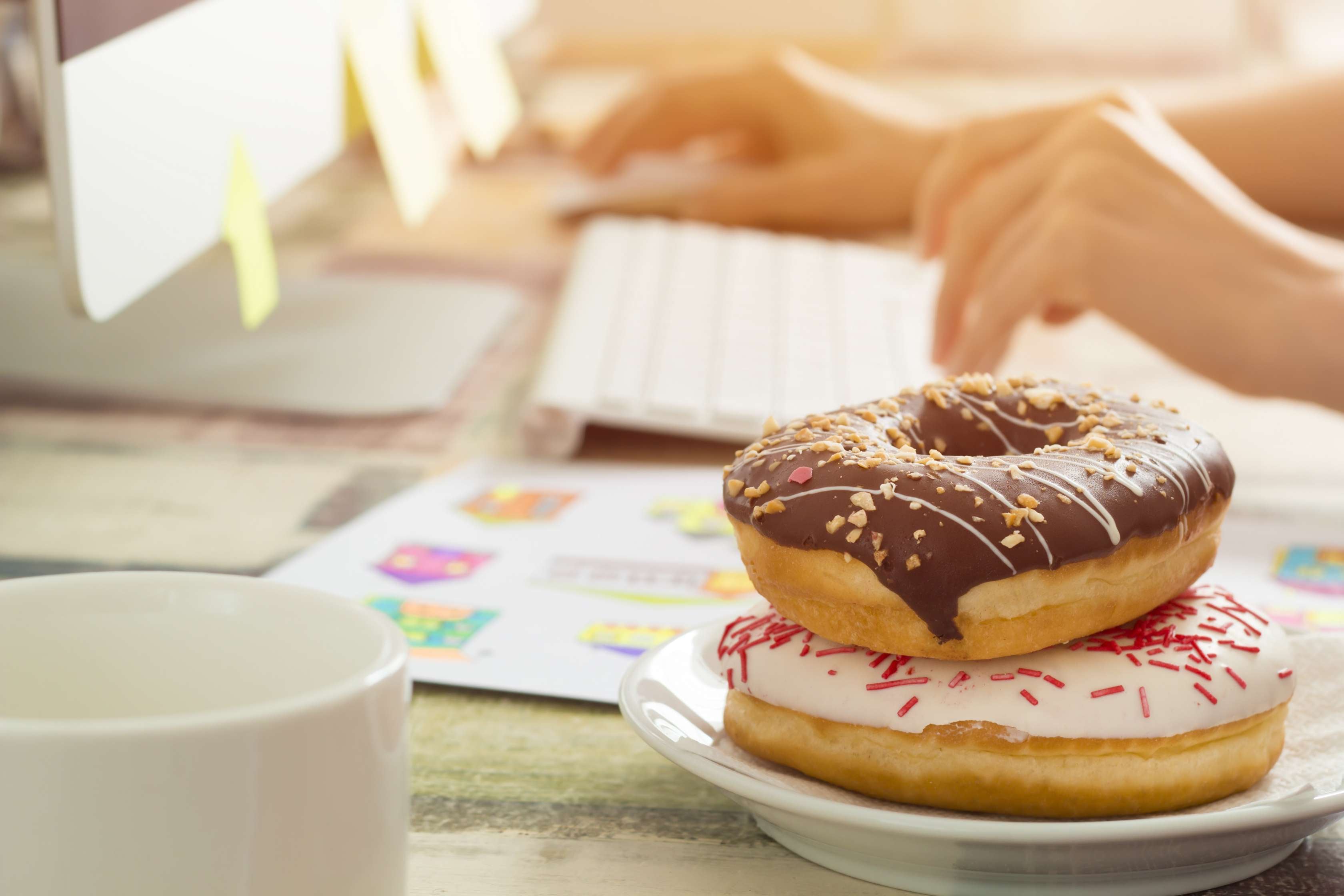 Allianz Gesundheitswelt - Raus aus der Zuckerfalle: auf einem Teller liegen zwei Donuts mit Glasur übereinander. Im Hintergrund sind eine Tastatur und ein Bildschirm zu erkennen.