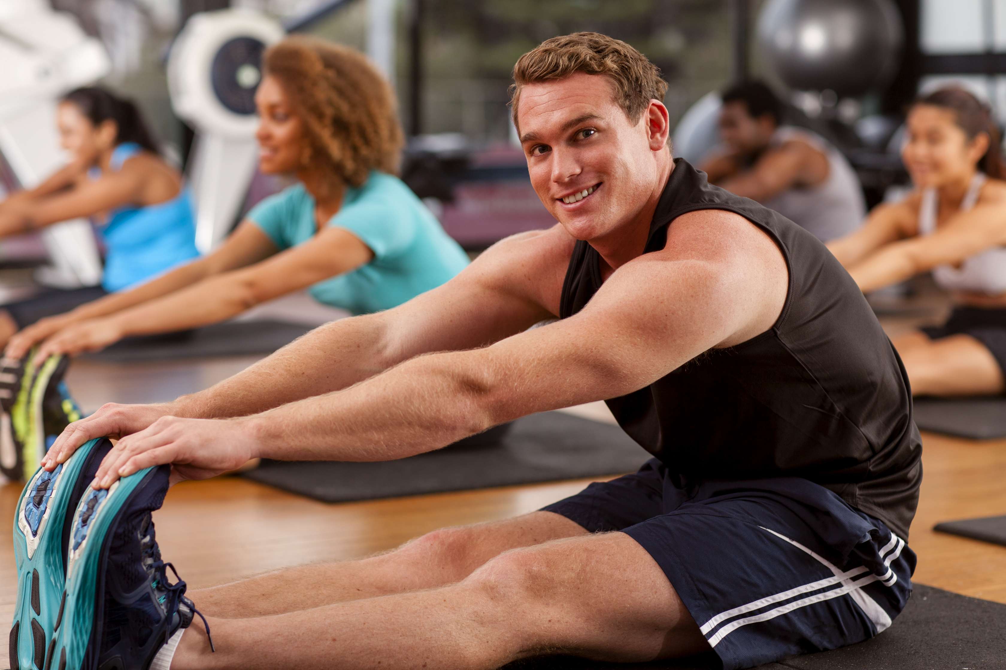 Allianz Gesundheitswelt - Rückenprgramm dehnen: ein junger Mann sitzt im Gym und dehnt seine Muskulatur, um sich auf seine Sporteinheit vorzubereiten.