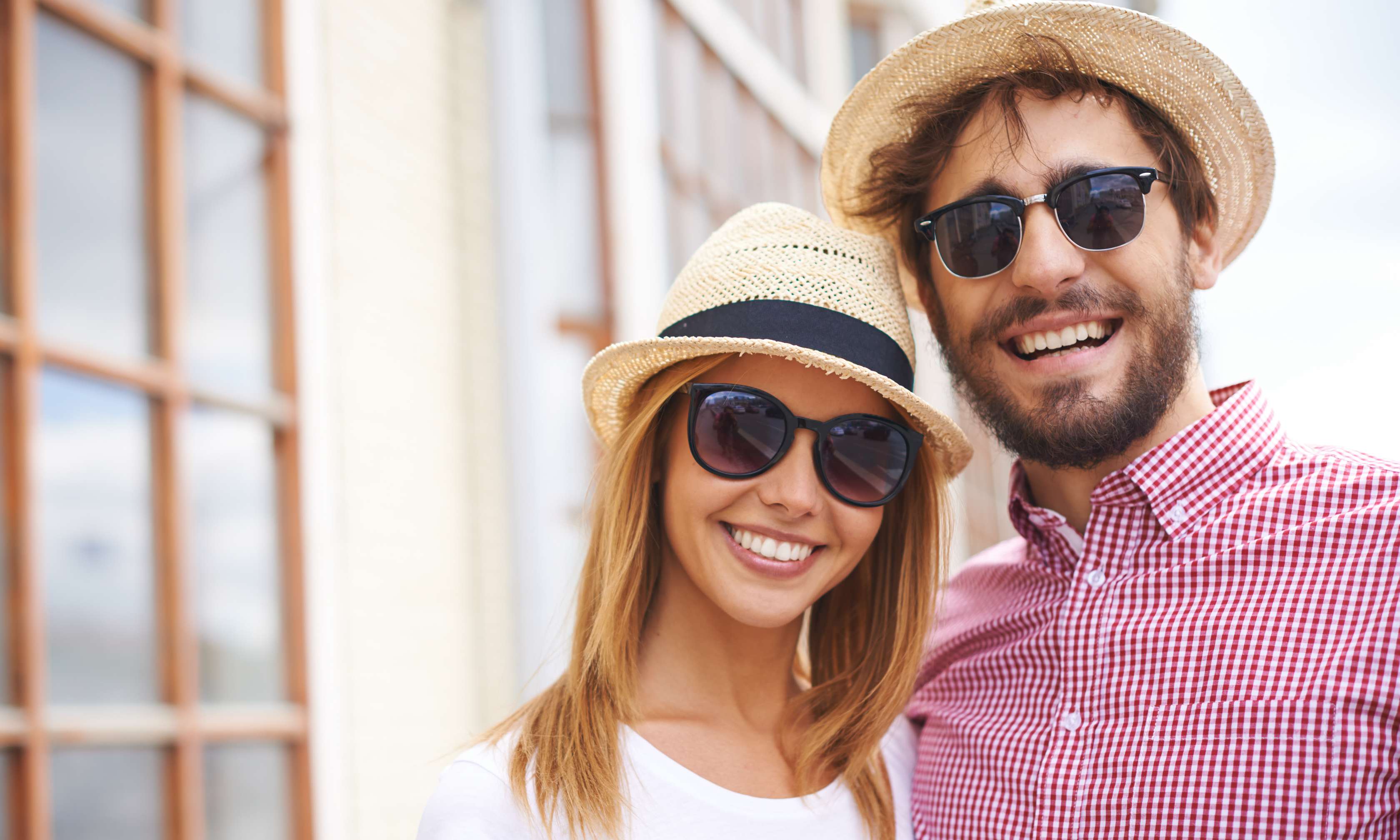 Allianz Gesundheitswelt - Schutz Sonnenbrillen: Ein Paar lacht in die Kamera. Sie tragen Sonnenhüte und Sonnenbrille, um sich vor der Sonne zu schützen.