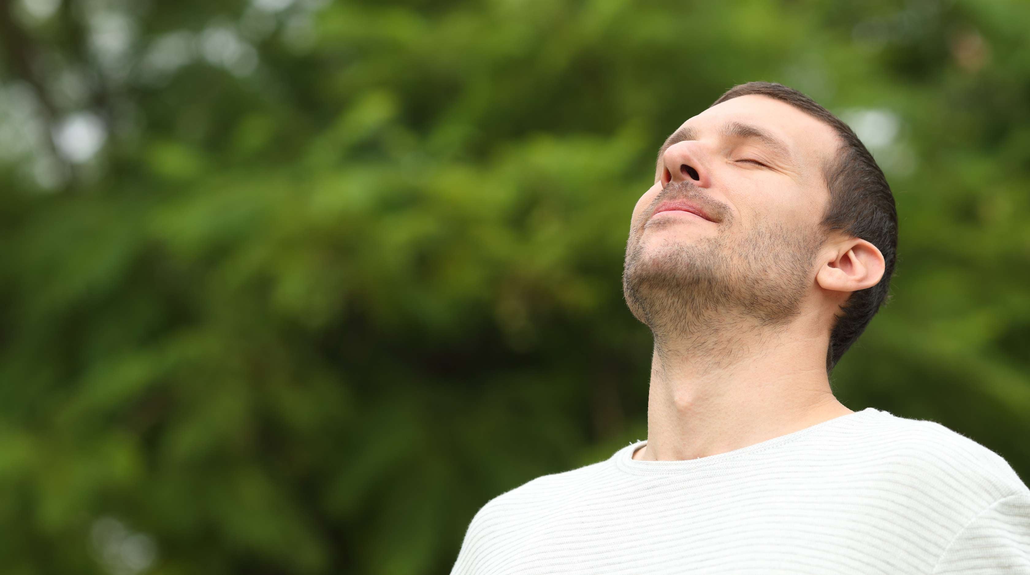 Allianz Gesundheitswelt - Stress abbauen: ein junger amnn steht mit geschlossenen Augen in der Natur und legt seinen Kopf in den nacken.