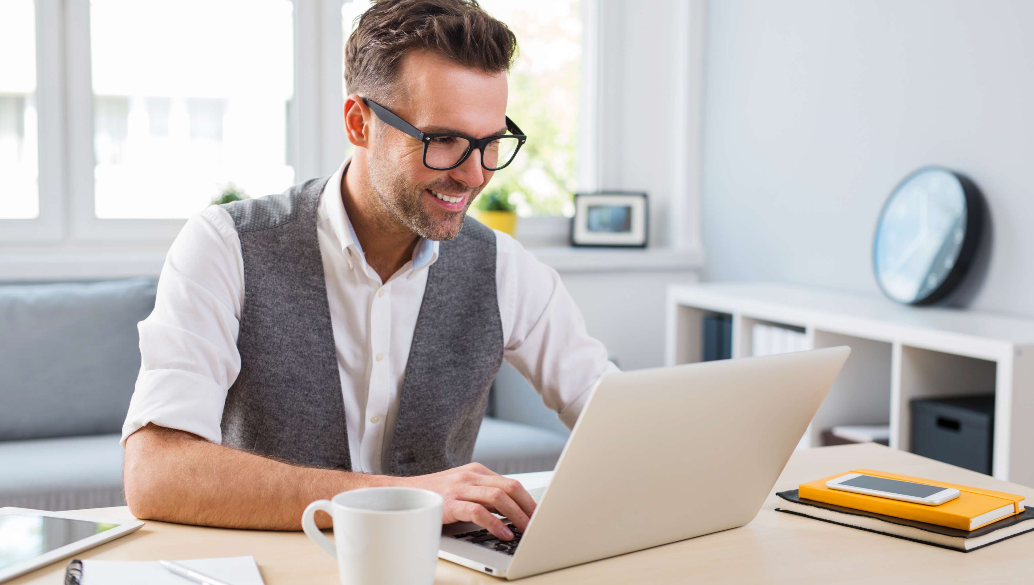 Allianz Gesundheitswelt - Tipps Homeoffice: Ein Mann mit weißem Hemd und grauer Weste sitzt im Homeoffice und arbeitet an seiunem Laptop.