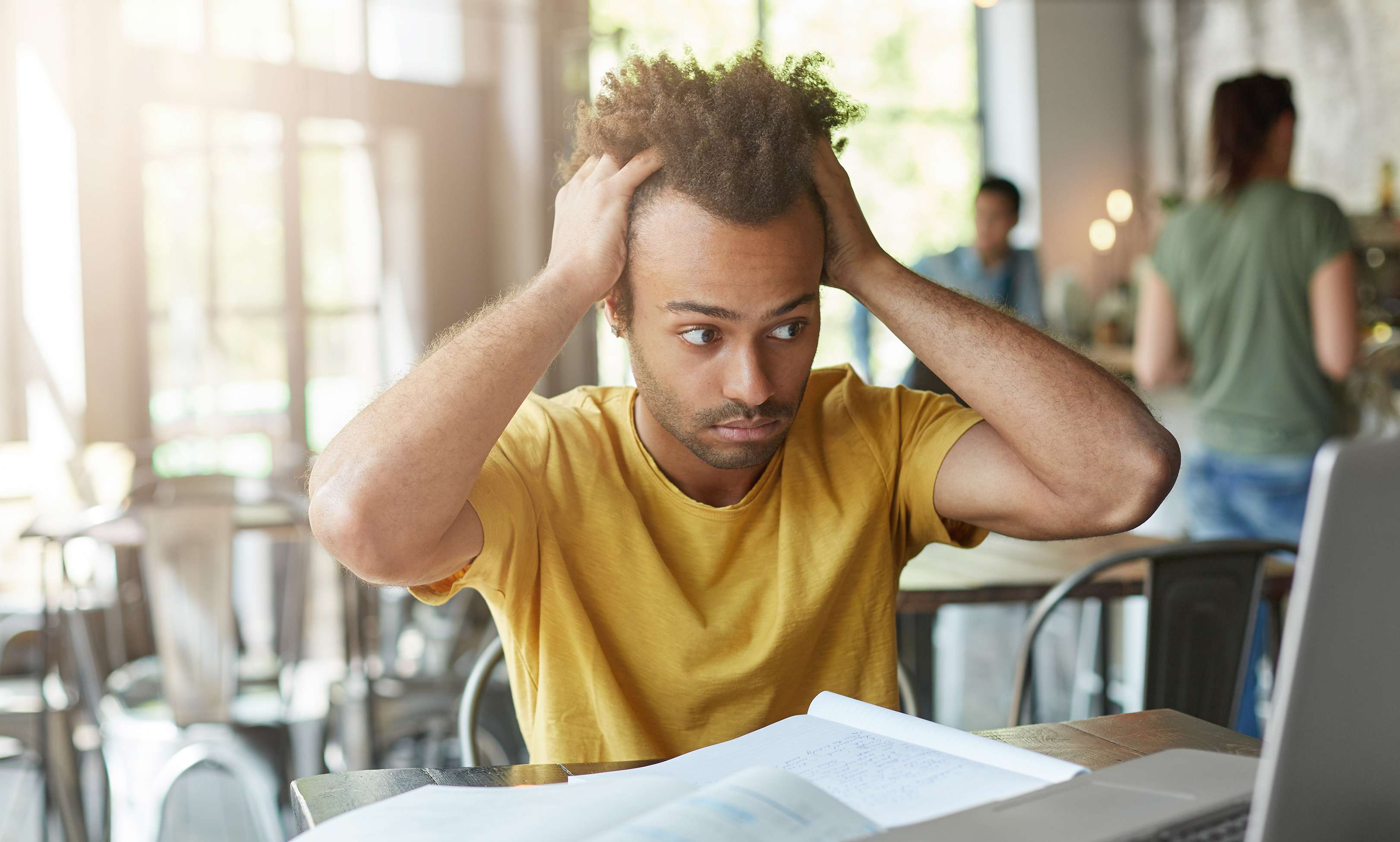 Allianz Gesundheitswelt - Tipps gegen Burn-out: ein junger Mann mit starken Locken sitzt im Café. Er rauft sich die Haare und sieht frustriert auf seinen Laptop.