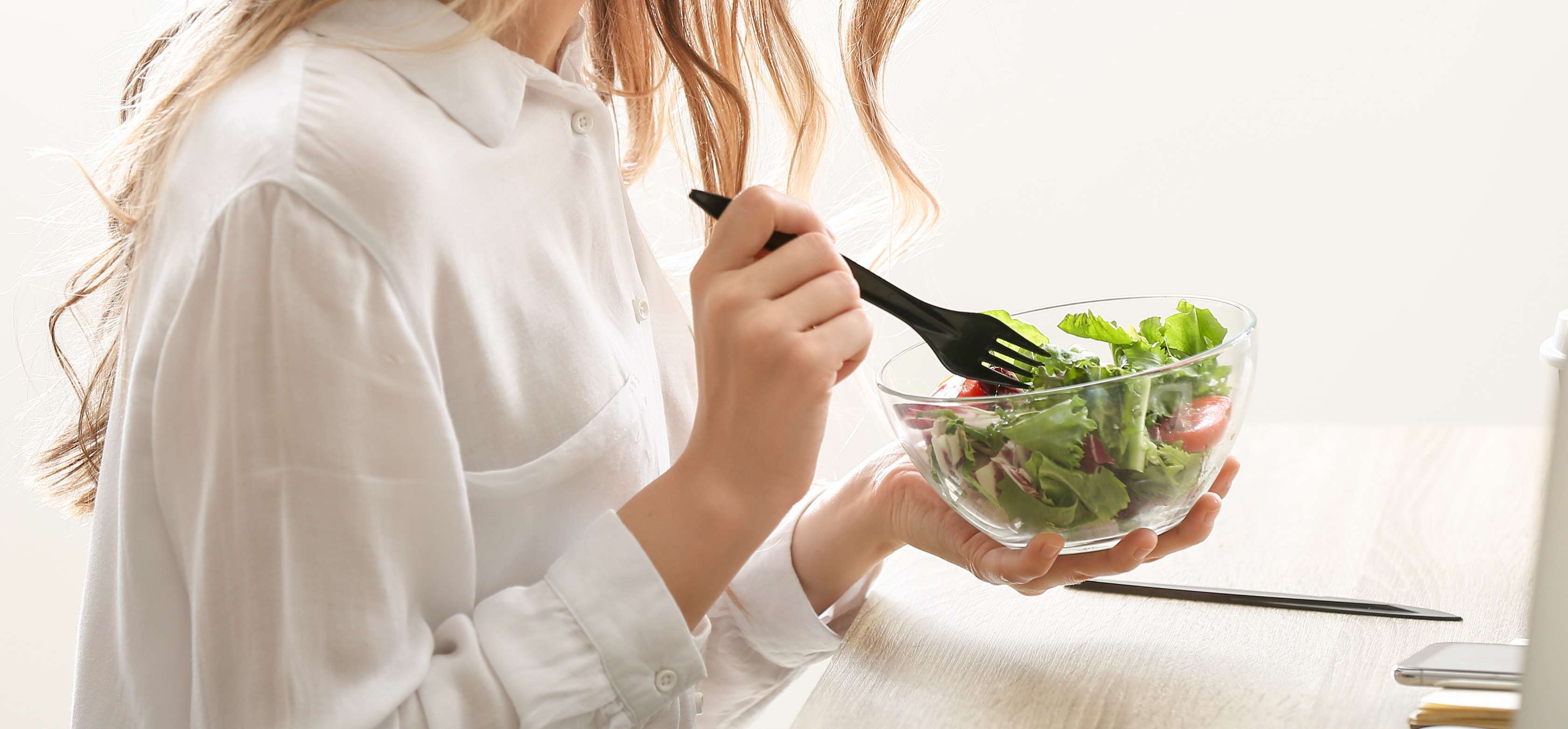 Allianz Gesundheitswelt - vegetarische Pausensnacks: Eine junge Frau mit blonden welligen Haaren isst an ihrem Schreibtisch einen gemischten Salat.