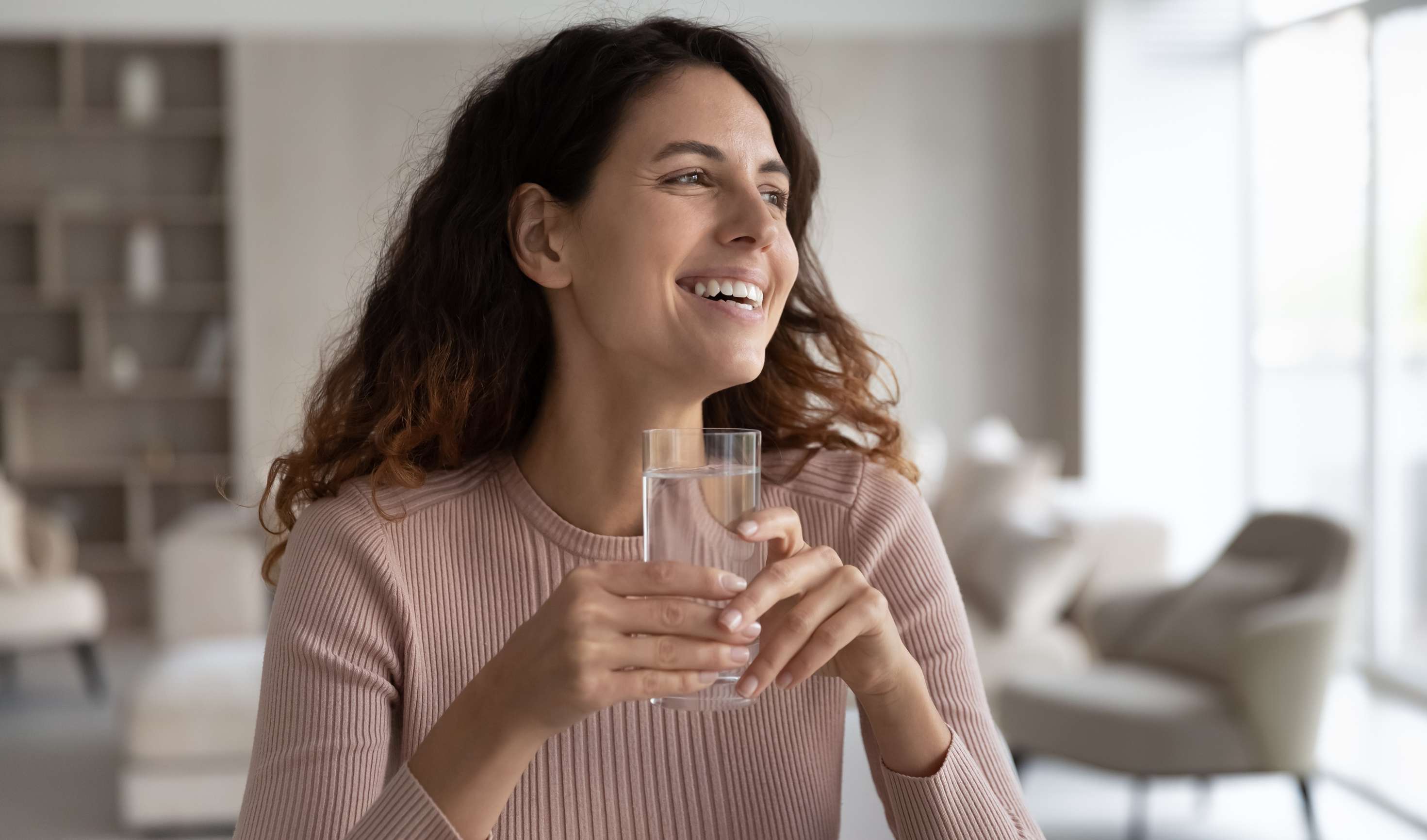 Allianz Gesundheitswelt - Fasten: eine lächelnde Frau hält ein Wasserglas in der Hand