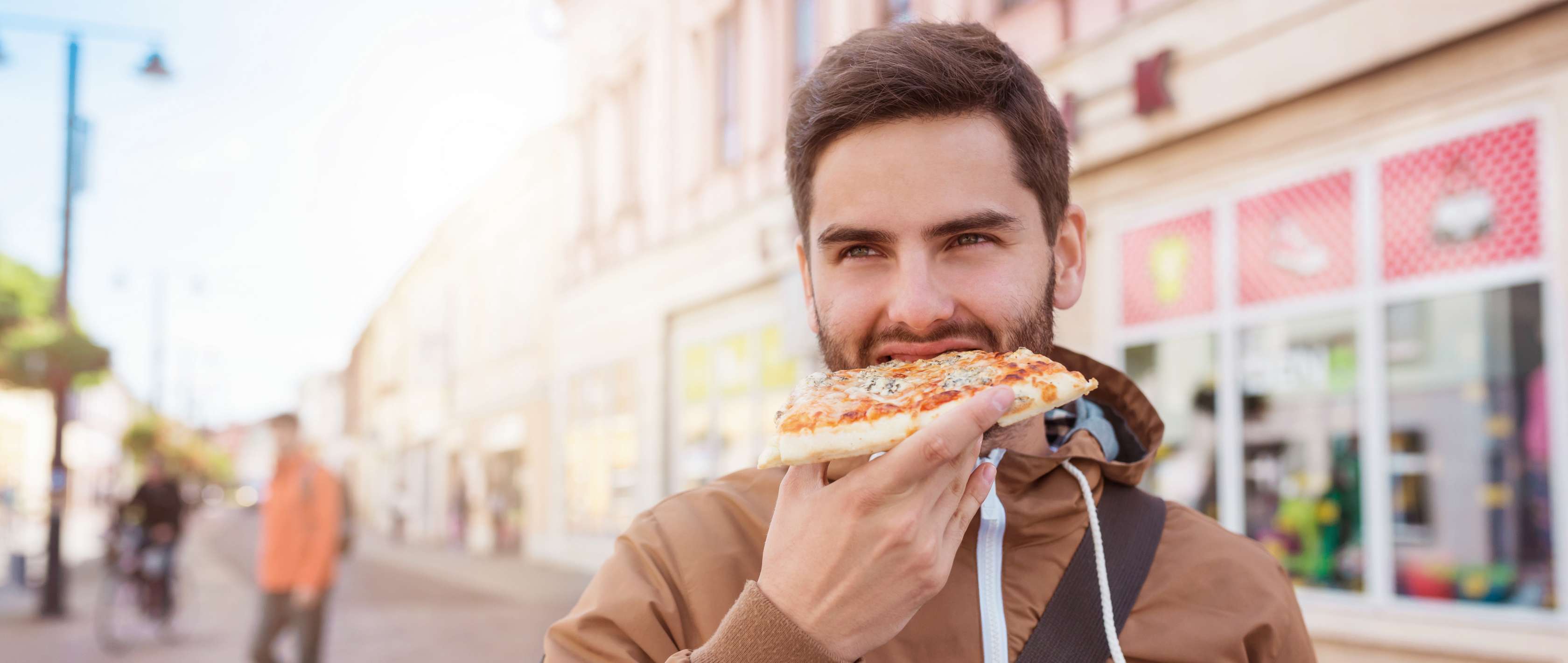 Allianz Gesundheitswelt - versteckter Zucker: ein junger Mann beißt in ein Stück Pizza.