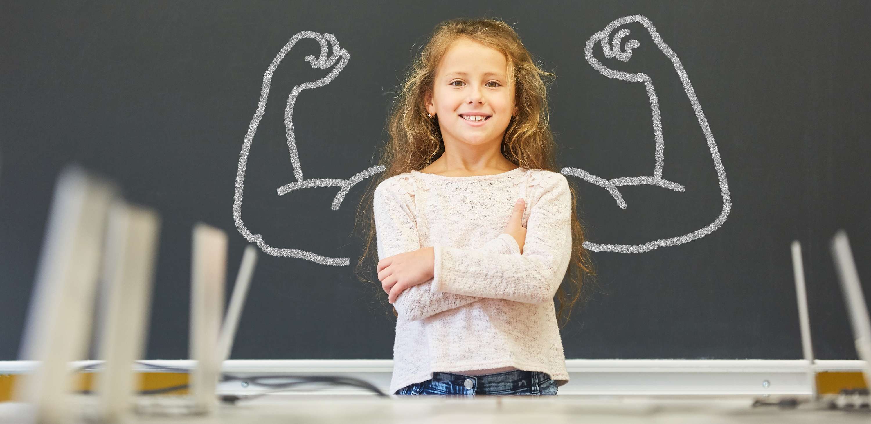 Allianz Gesundheitswelt - mentale Kindergesundheit stärken: ein Mädchen steht vor einer Tafel, auf der muskulöse Arme aufgezeichnet sind