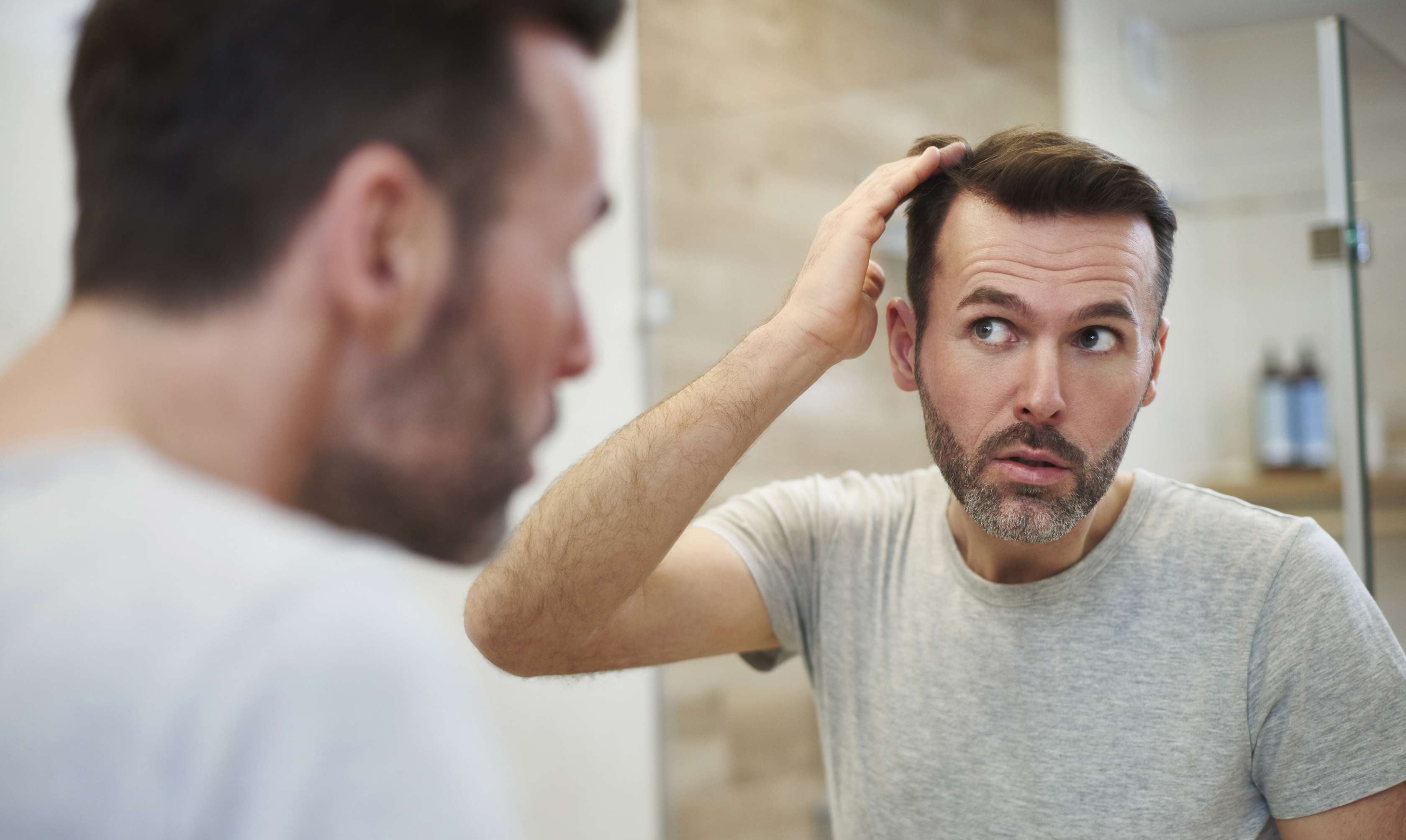 Allianz Gesundheitswelt - Wechseljahre beim Mann: Ein Mann steht vor dem Spiegel und sucht nach grauen Haaren.