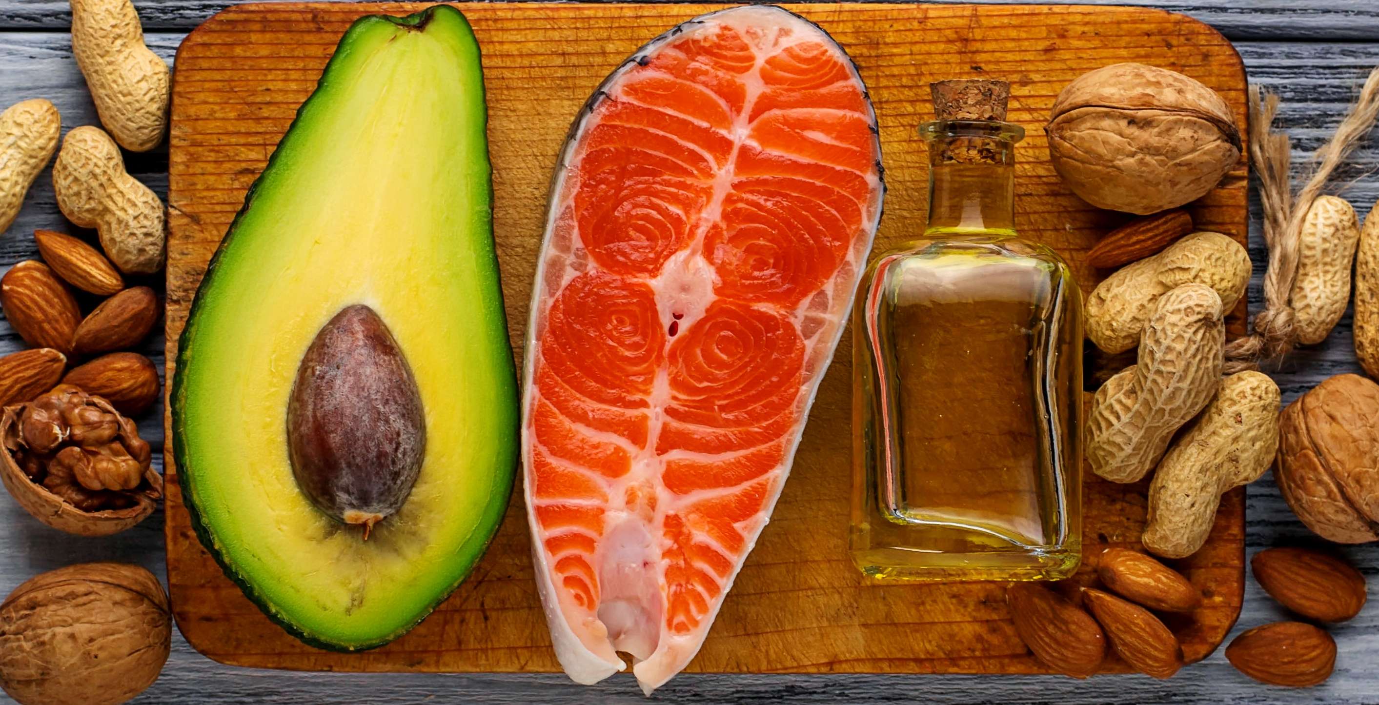 Allianz Gesundheitswelt - Gesünder mit Fett: Verschiedene Lebensmittel mit vielen Fetten - darunter Avocado, Lachs und Nüsse - liegen auf einer Arbeitsplatte.