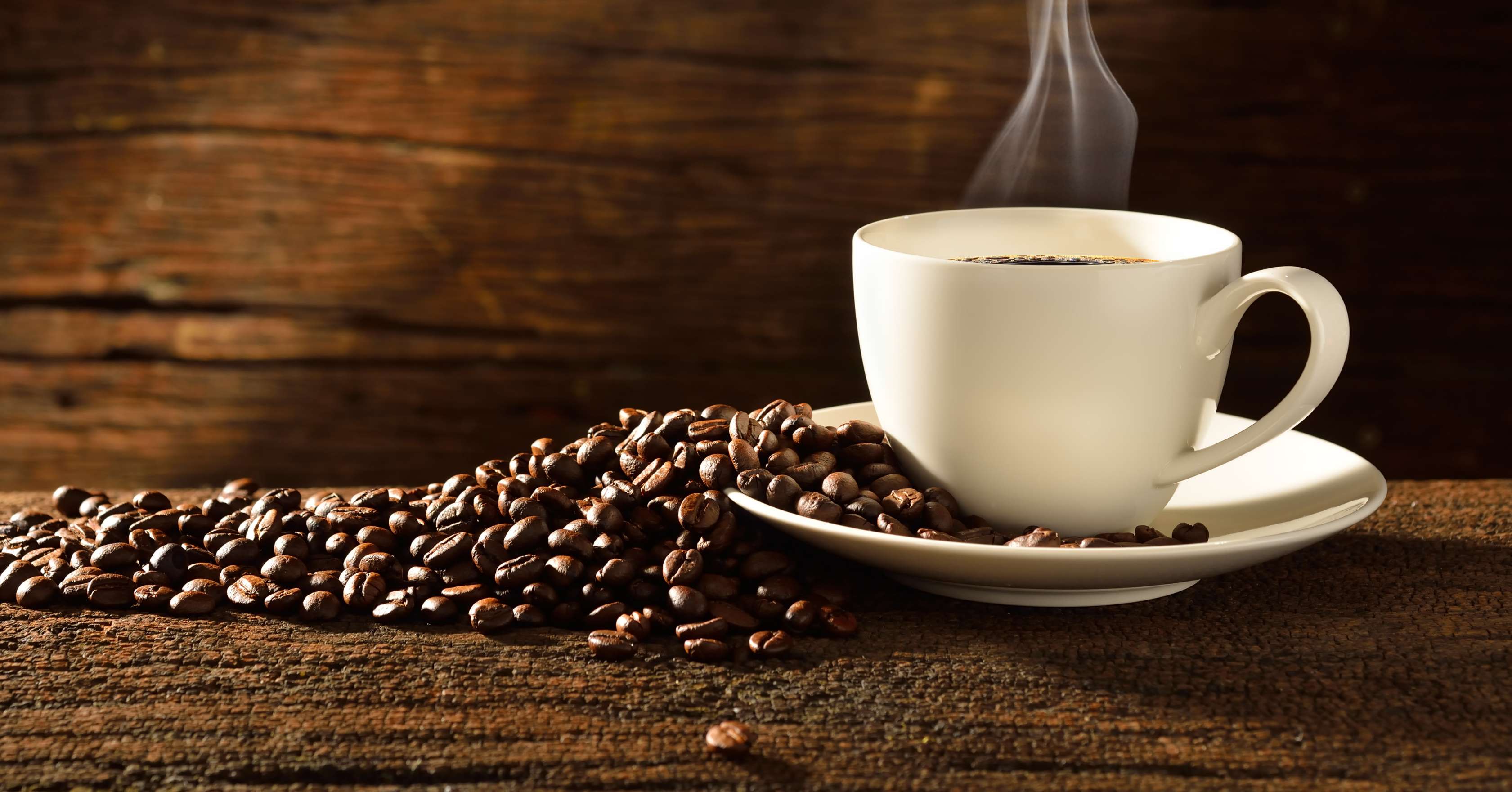 Allianz Gesundheitswelt - Kaffee: Eine weiße Tasse mit Kaffee steht  auf der rechten Seite. Links neben der Tasse sind Kaffeebohnen verteilt.