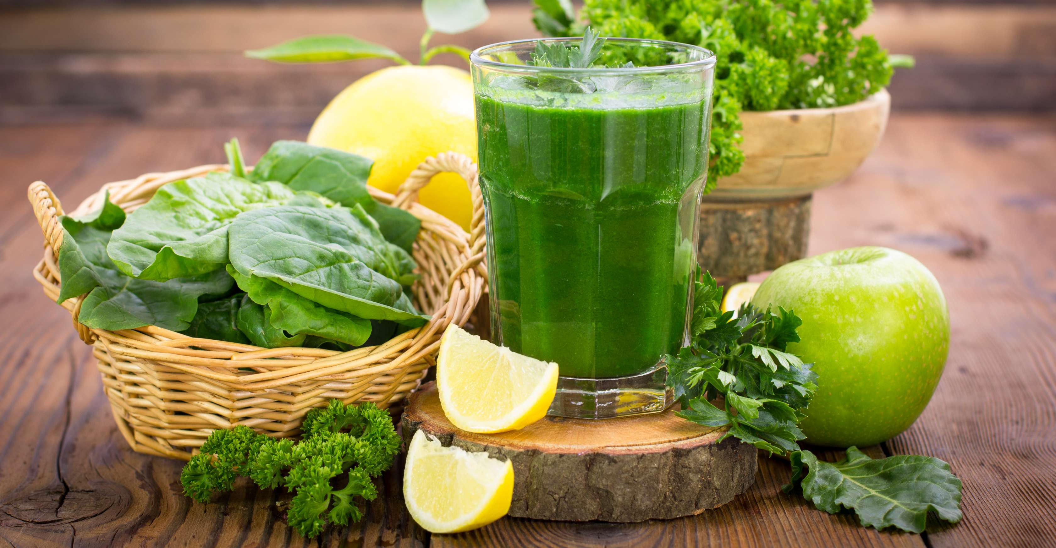 Allianz Gesundheitswelt - Smoothies: ein grüner Smoothie und seine Inhaltsstoffe - Apfel, Grünkohl, Zitrone und Petersilie - stehen auf einem Holzbrett.