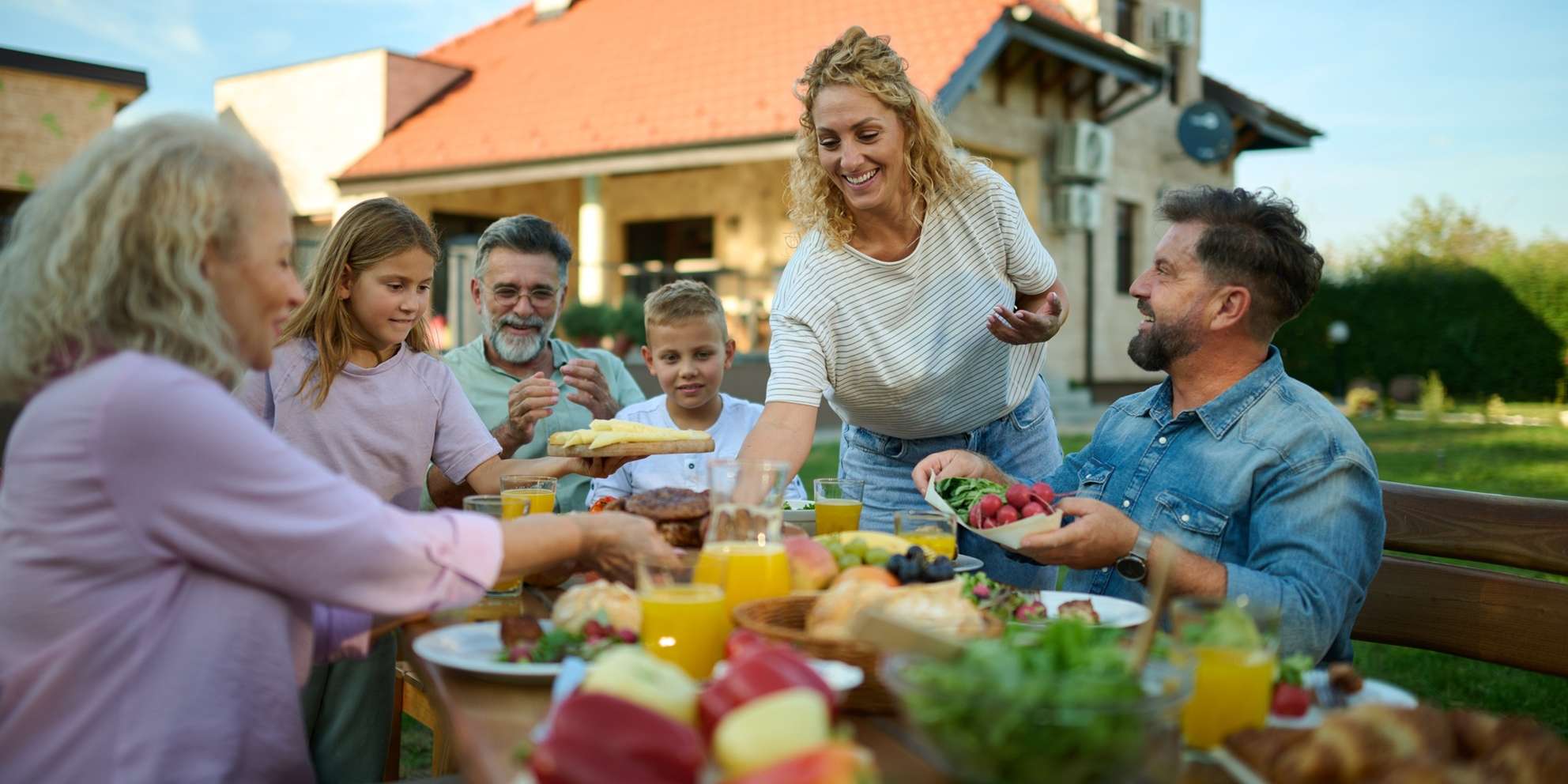 Allianz Gesundheitswelt – Sommerküche: Familie sitzt beim Essen im Garten.
