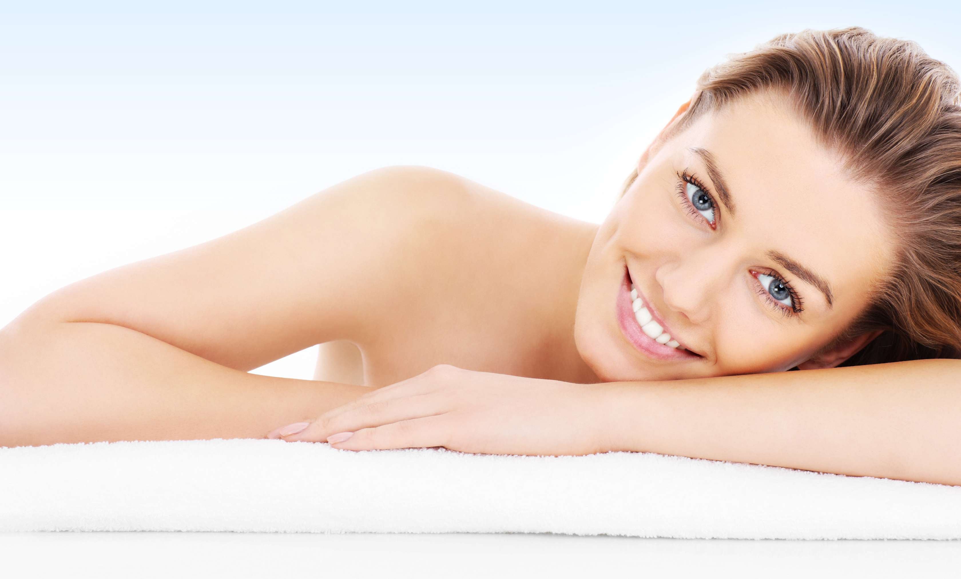 Allianz Gesundheitswelt - Sinnesorgan Haut: eine junge Frau liegt mit ihrem Kopf seitlich auf ihrem rechten Unterarm und lächelt in die Kamera.