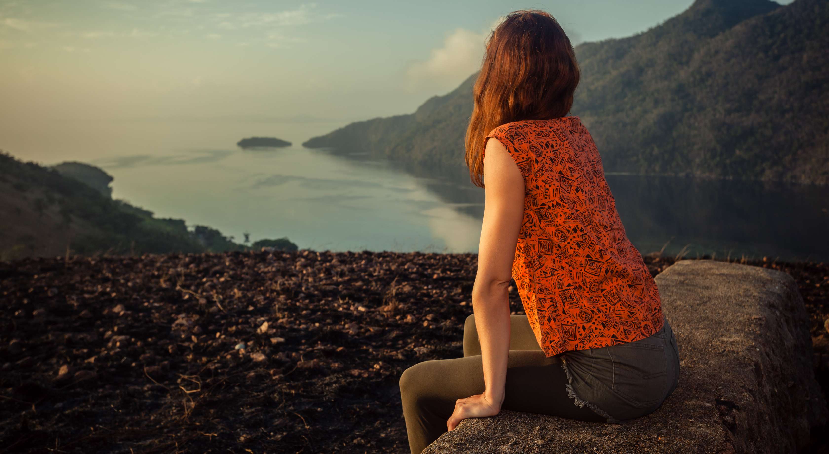 Allianz Gesundheitswelt - Seelische Gesundheit: Frau sitzt auf einem Stein und schaut dem Horizont entgegen