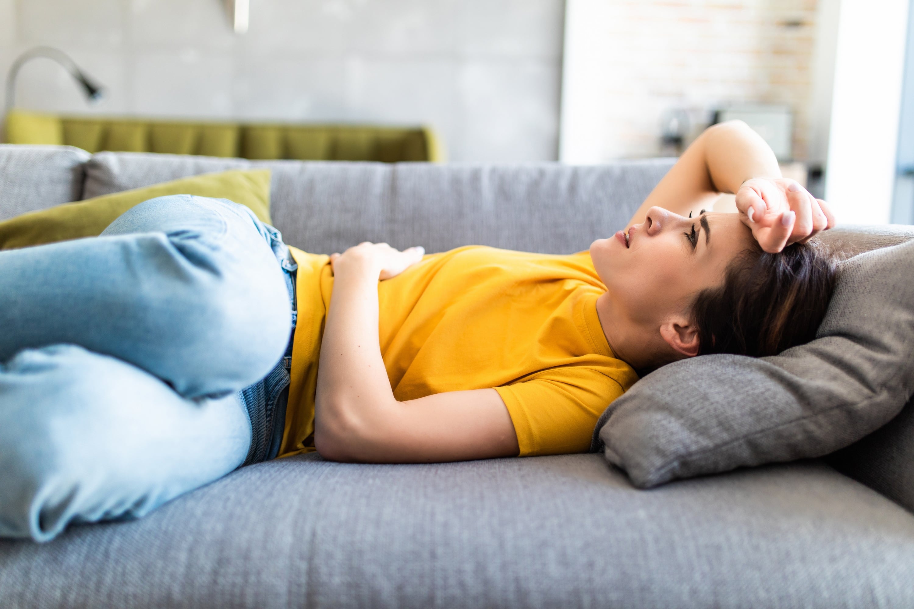 Eine Frau liegt einem Sofa und hat sichtlich Kopfschmerzen