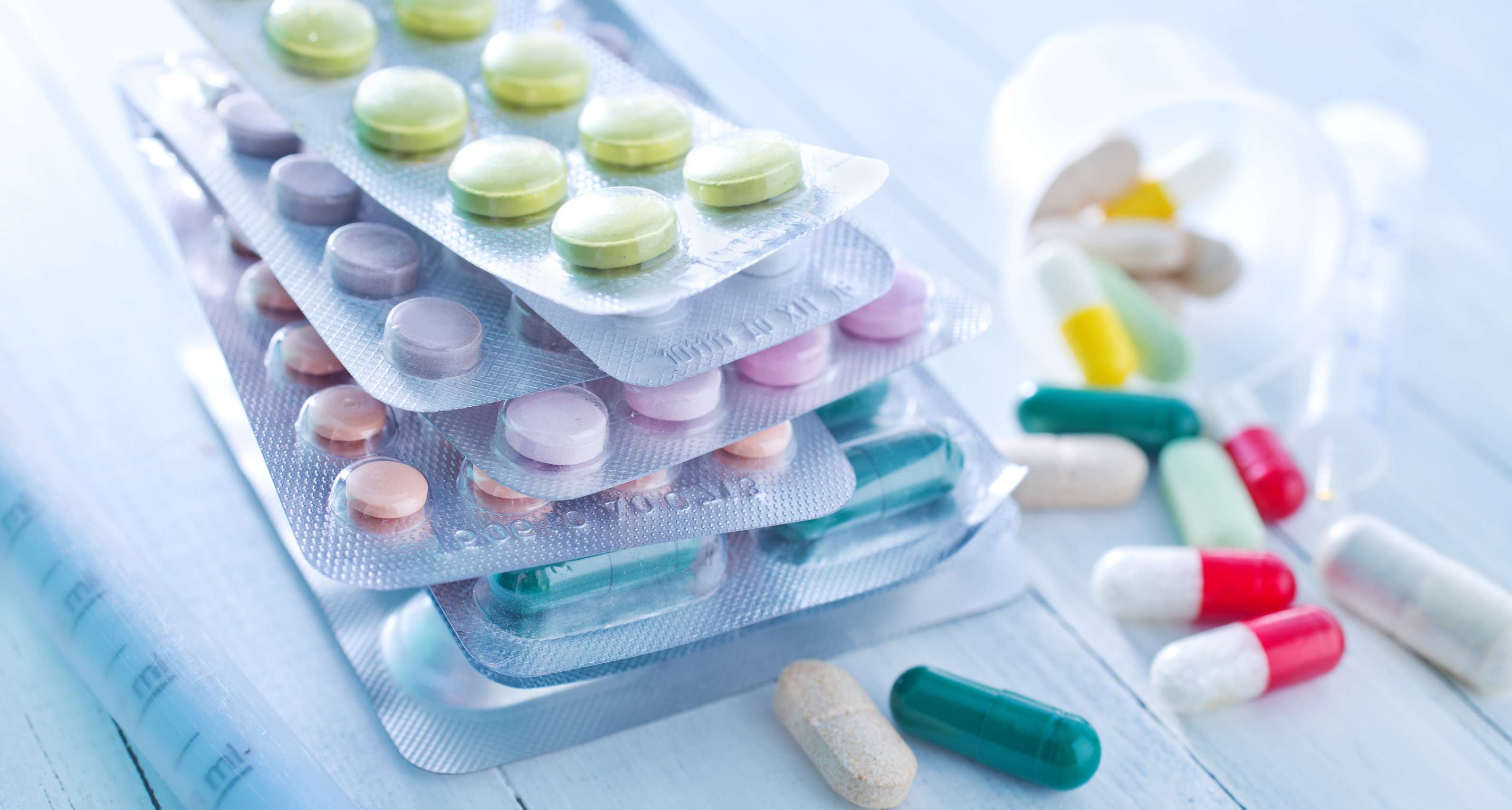 Allianz Gesundheitswelt - Arzneimittelkosten: Verschiedene Medikamentenblister und bunte Pillen auf einer Arbeitsfläche