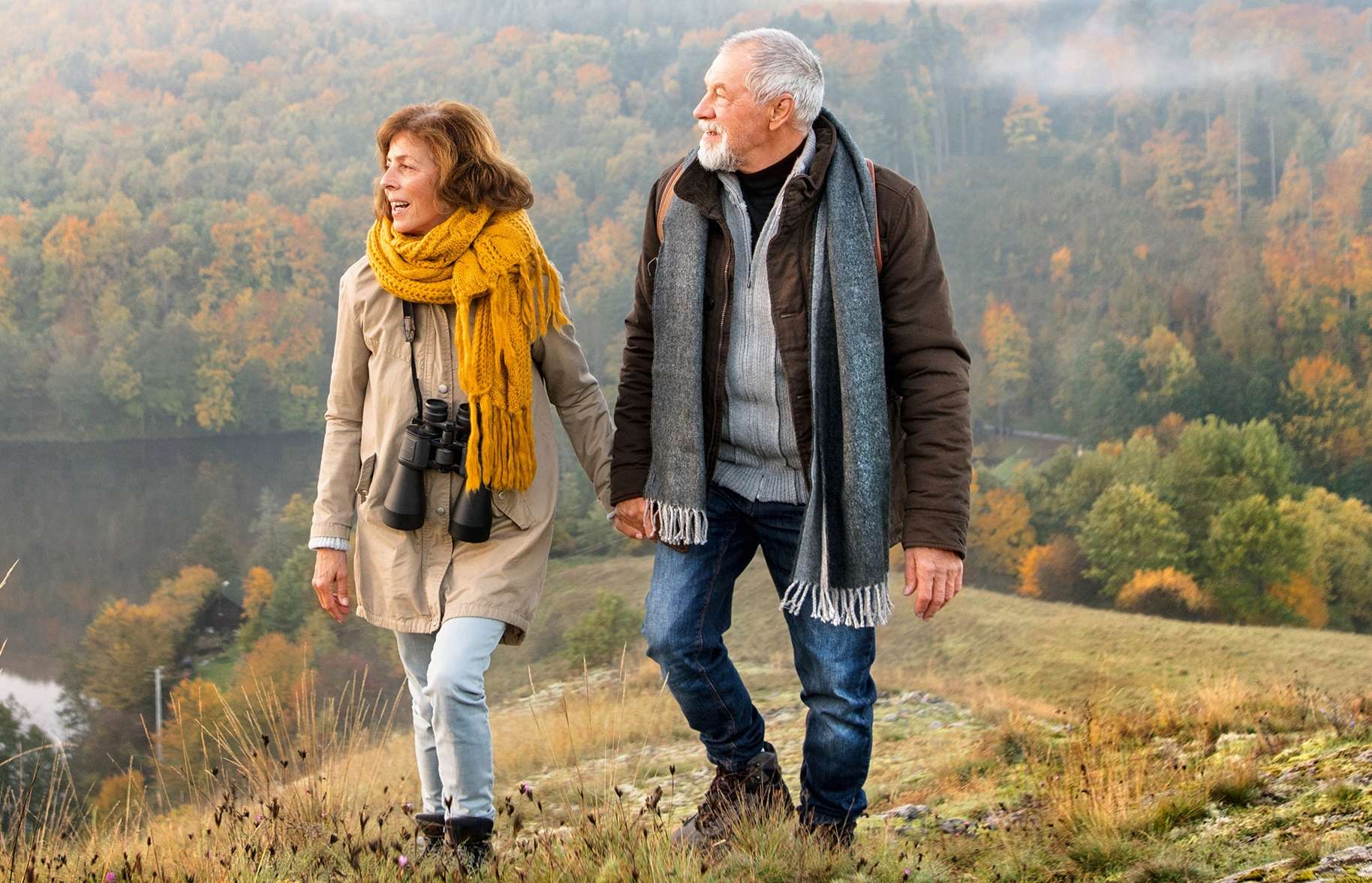 Allianz Gesundheitswelt - Leben mit Arthrose: ein älteres Paar mit Übergangsjacken wandert durch eine herbstliche Landschaft.