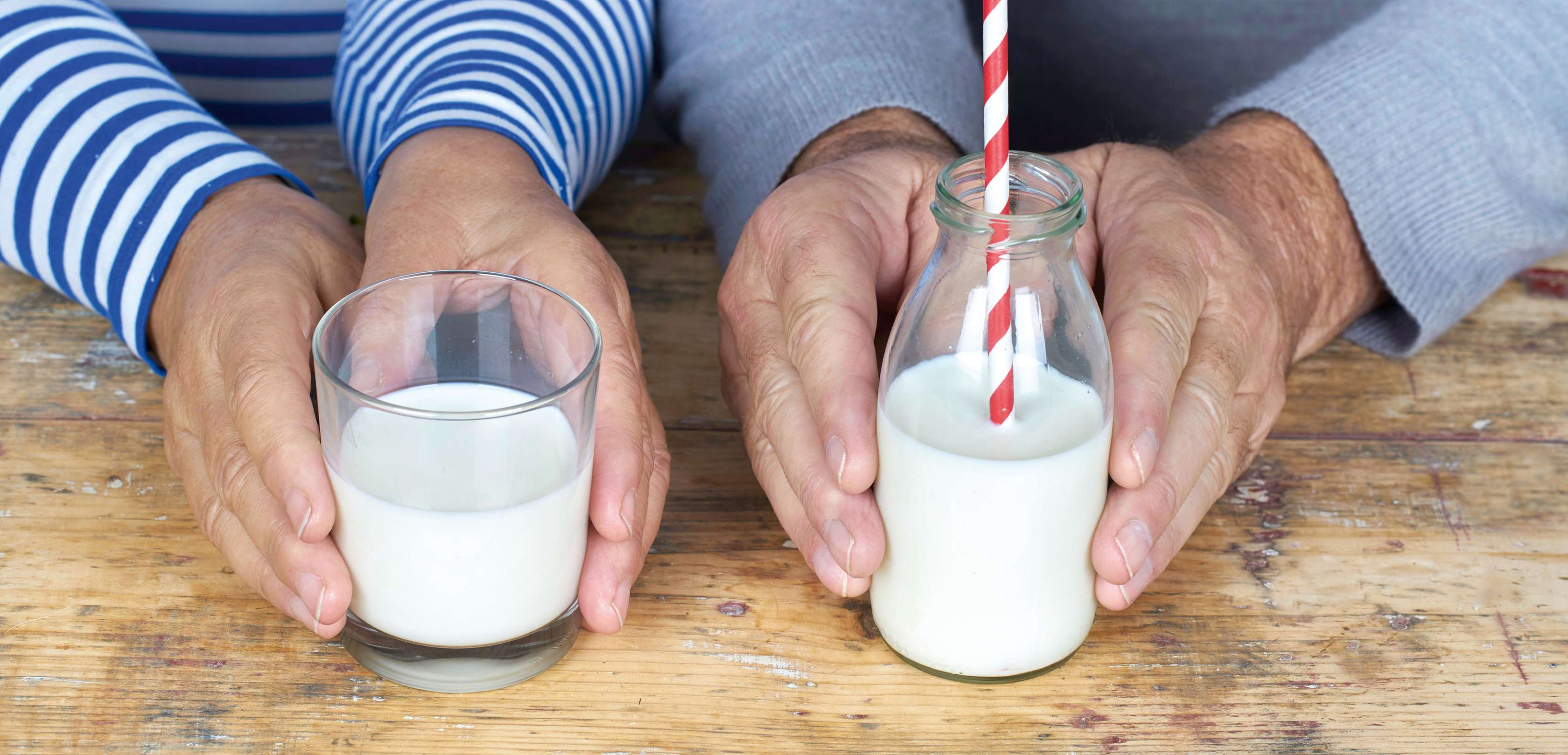 Allianz Gesundheitswelt - was ist Osteoporose: auf einer Arbeitsplatte stehen zwei Gläser mit Milch. Beide Gläser werden von älteren Personen gehalten.