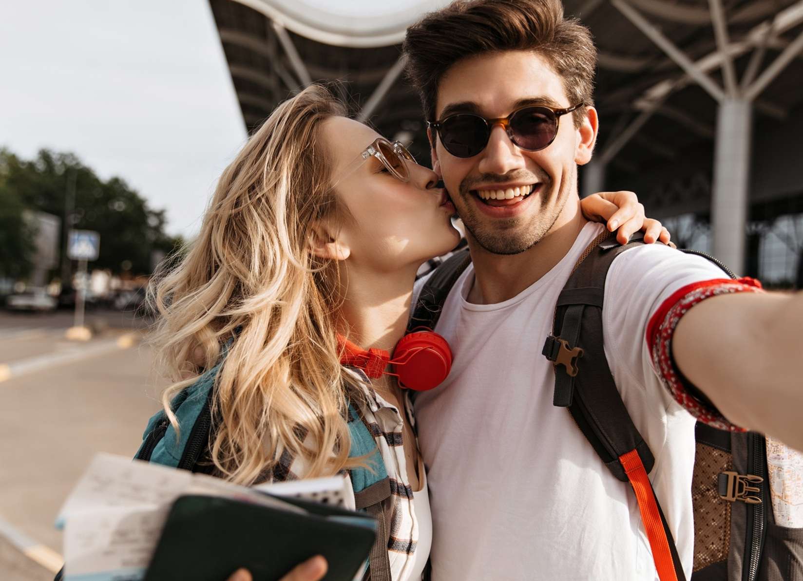 Allianz Gesundheitswelt - Sonnenbrille mit UV-Schutz: Ein Paar mit Sonnenbrillen, er lacht in die Kamera., während sie ihm einen Kuss auf die Wange gibt.