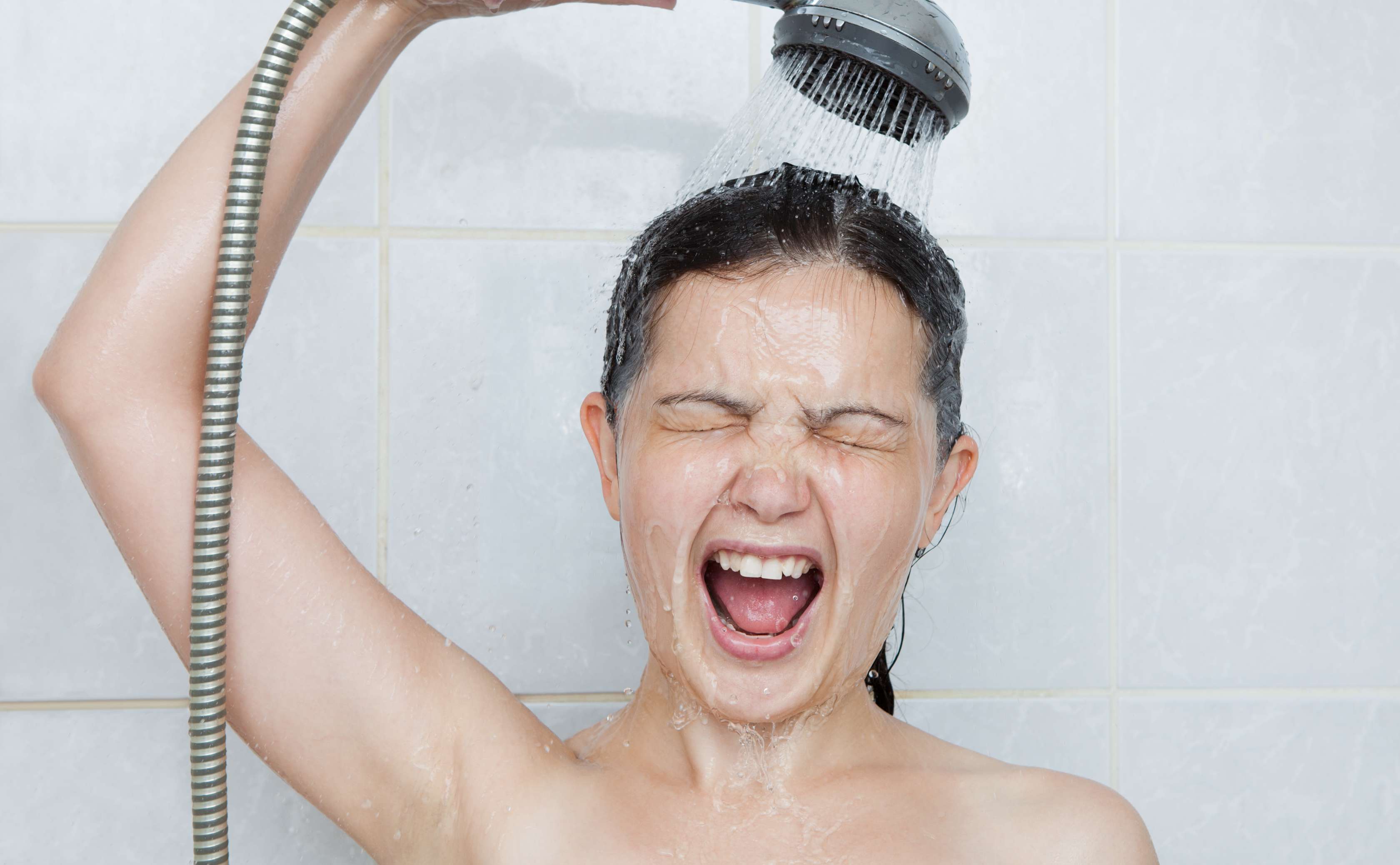 Allianz Gesundheitswelt - Wintermythen: eine junge Frau steht mit geschlossenen Augen und offenem Mund unter der Dusche und  lässt sich warmes Wasser über den Kopf laufen.