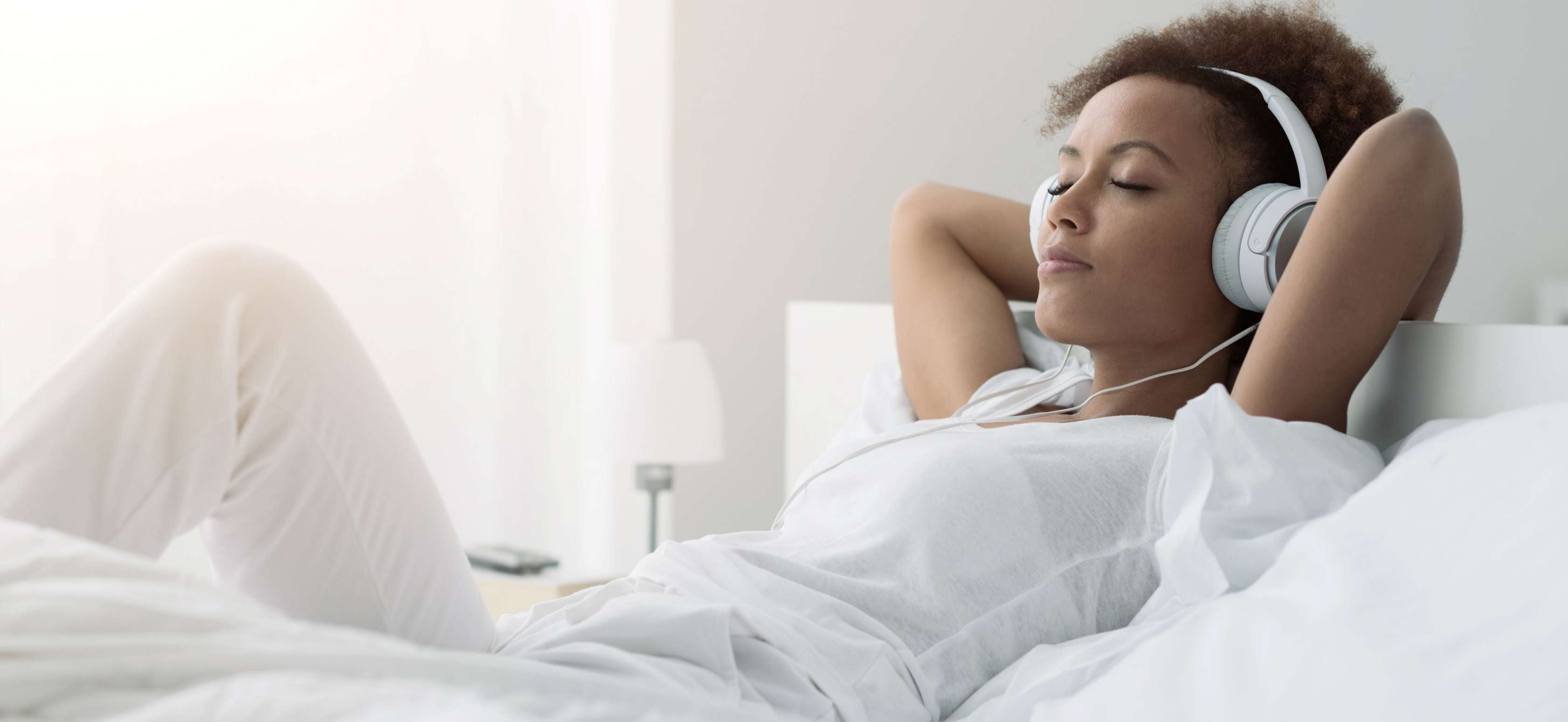 Allianz Gesundheitswelt - Musik hilft: eine junge Frau liegt auf einem Bett und hört über ihre Kopfhörer Musik.