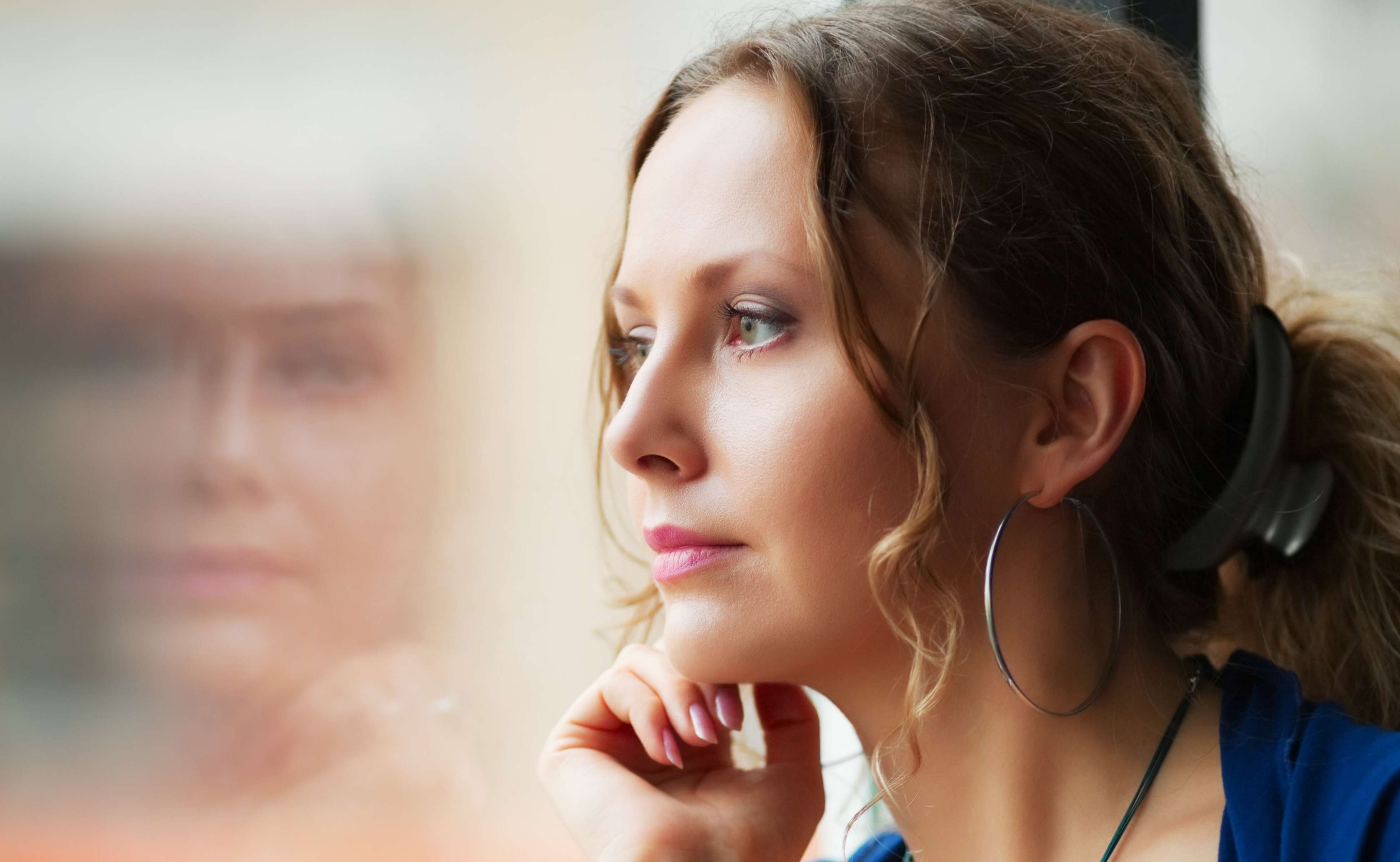 Allianz Gesundheitswelt - Stress und Burn-out: eine junge Frau sitzt am Fenster und sieht gedankenverloren nach draußen.