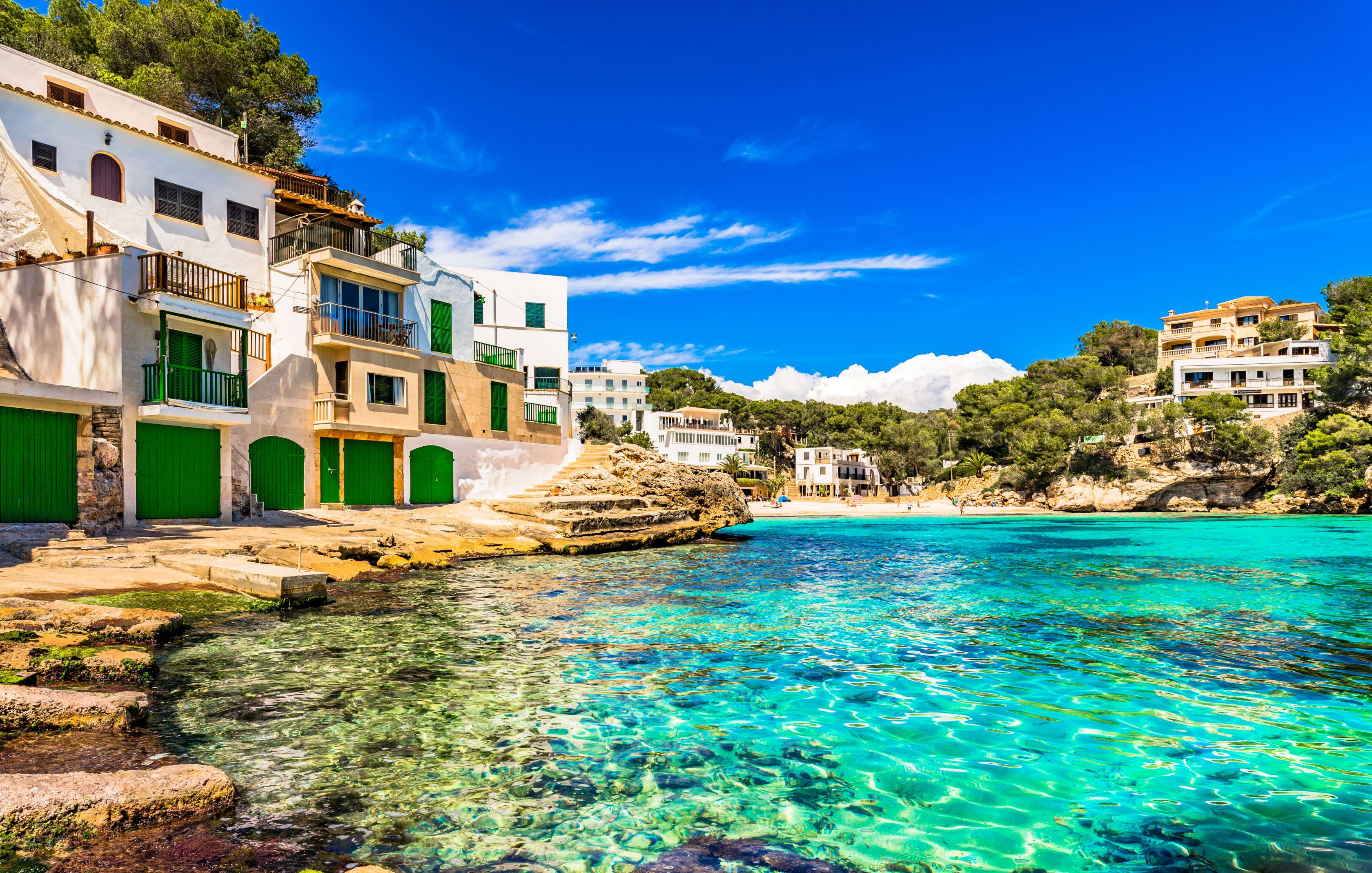 Allianz Gesundheitswelt - Reise und Freizeit: Blick in eine Bucht mit klarem, türkisenem Wasser. Links und rechts ist die Bucht von Felsen und südländischen Häusern umgeben.