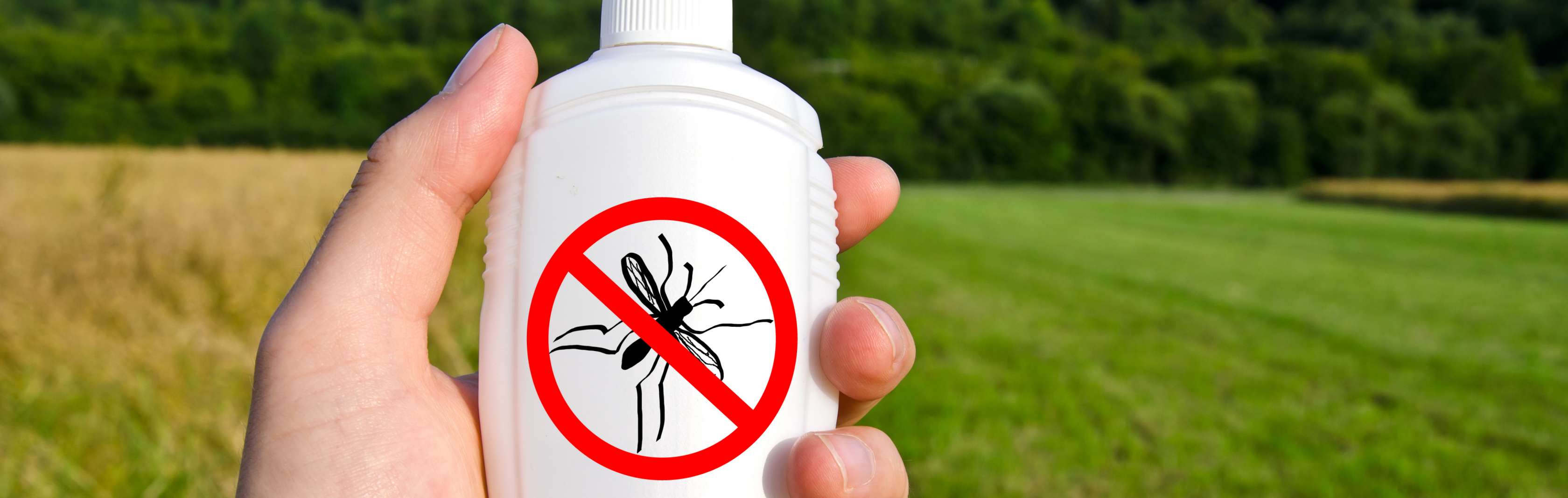 Allianz Gesundheitswelt - Tipps gegen Insekten: Eine Hand hält eine weiße Sprühflasche mit einem durchgestrichenen Insektenzeichen. Im Hintergrund sind Wiesen zu erkennen.