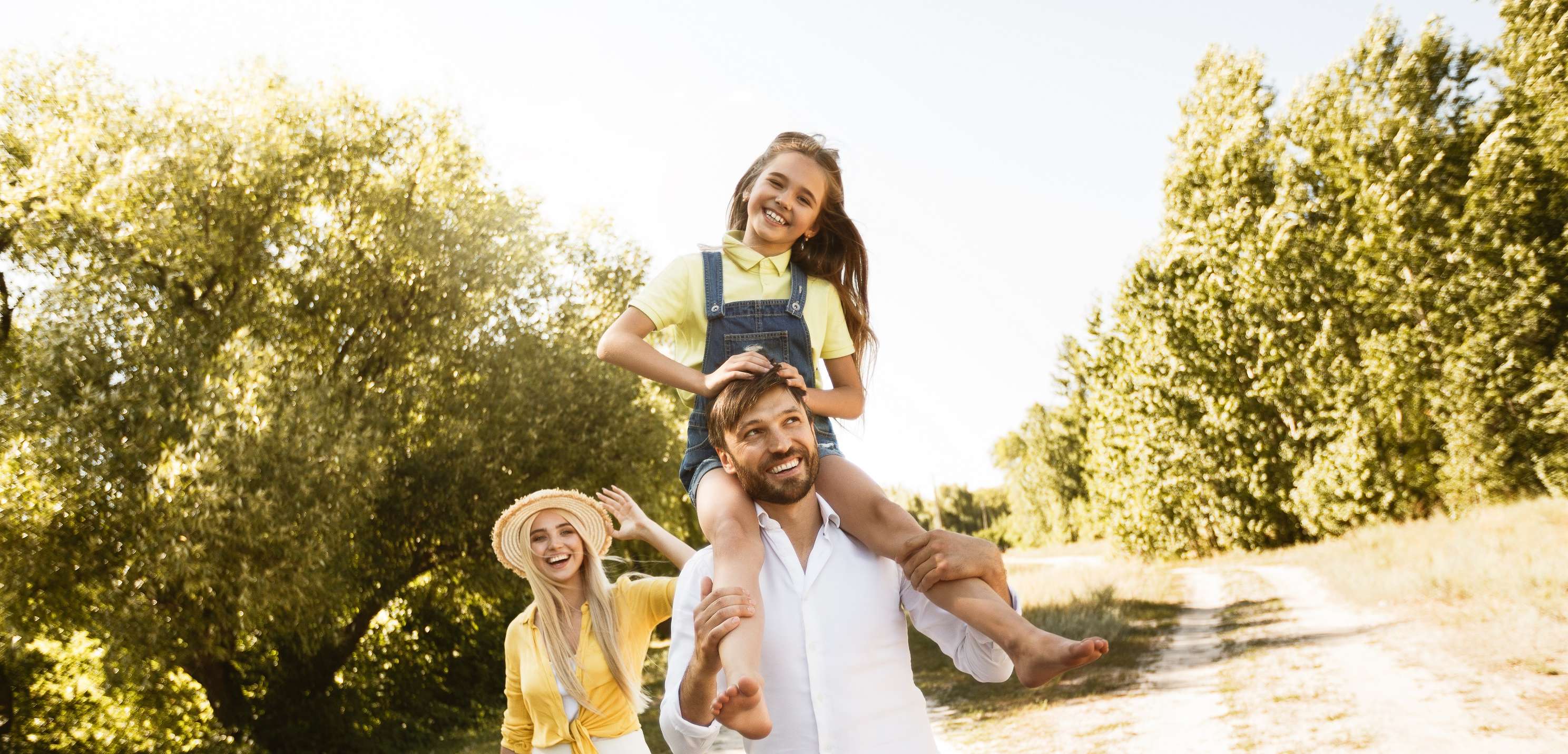 Allianz Gesundheitswelt - Allianz gegen Schmerz: eine Familie spaziert im Sommer durch die Natur. Das Mädchen sitzt auf den Schultern des Vaters.