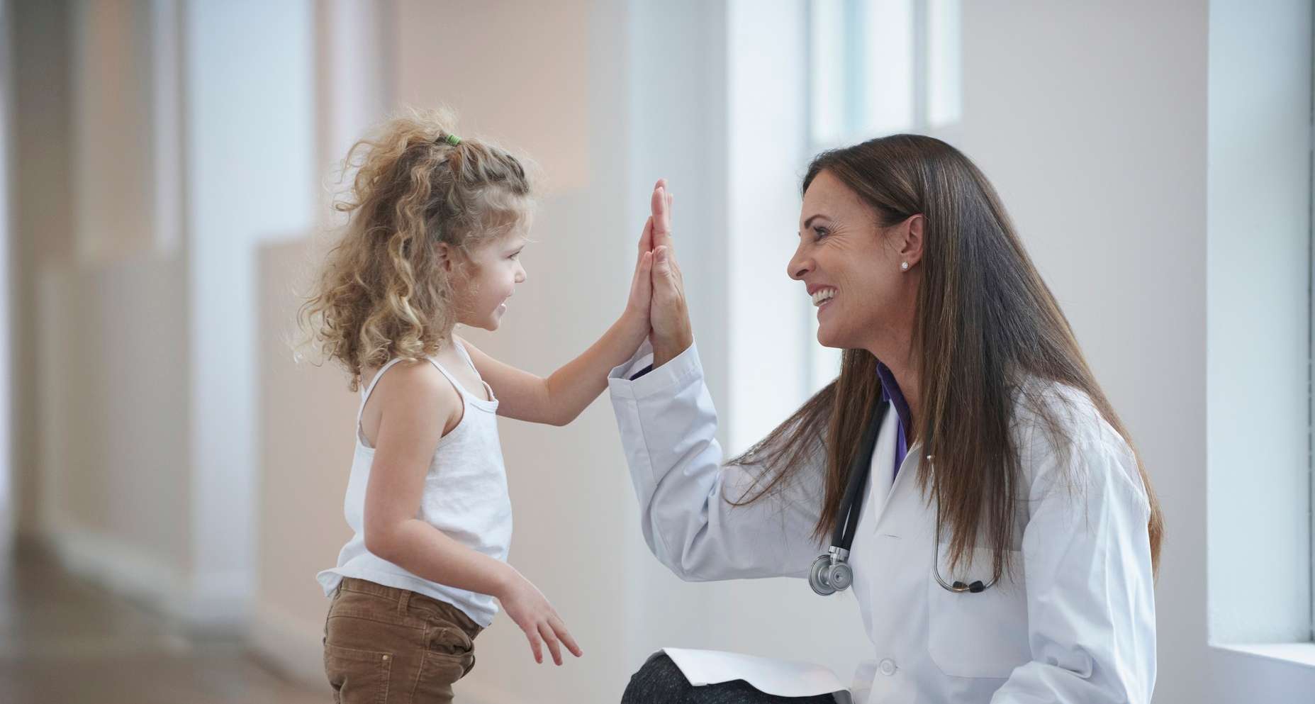 Allianz Gesundheitswelt - Arzt- und Kliniksuche: eine Ärzting mit langen dunklen Haaren gibt einer jungen Patientin ein High five.