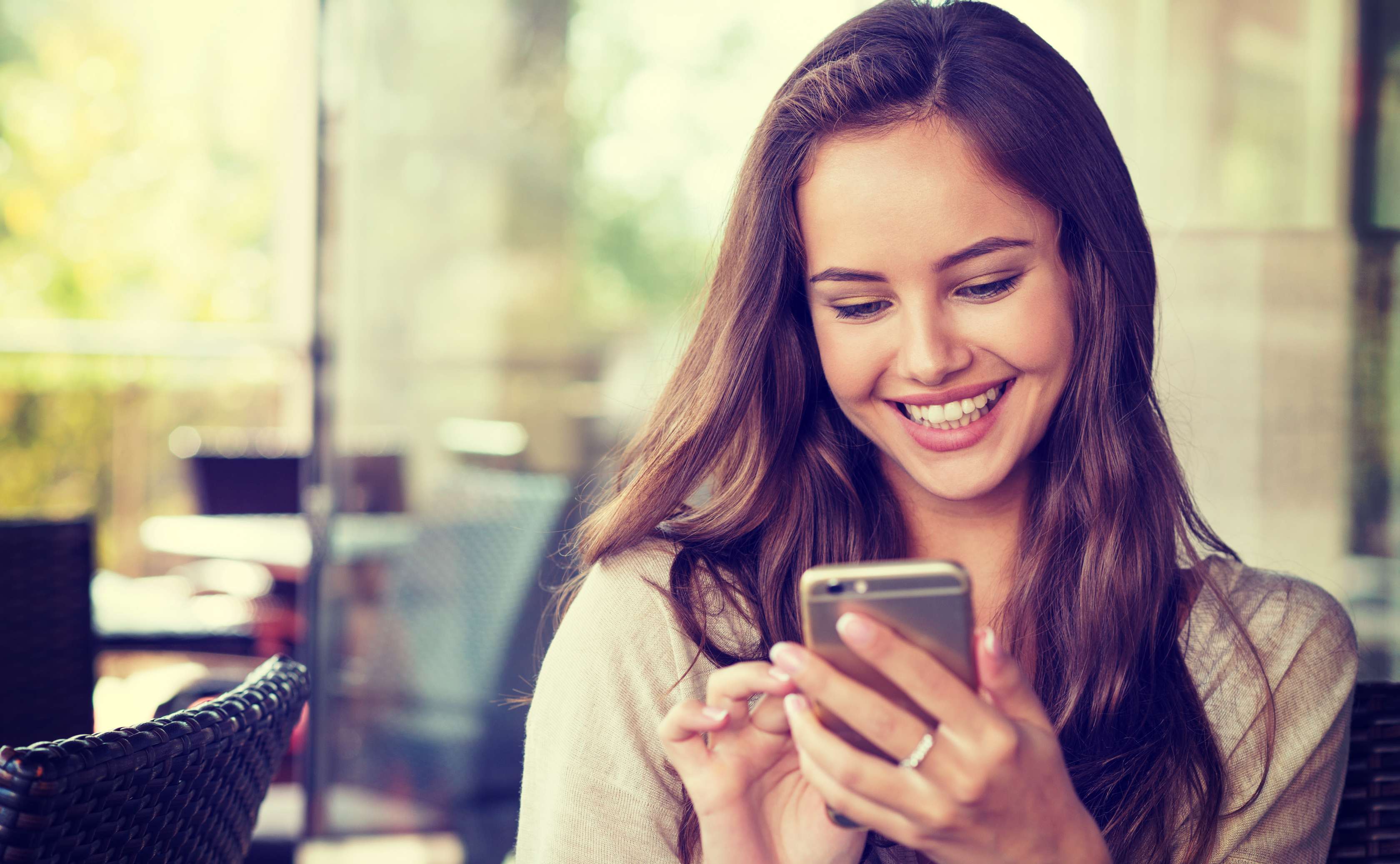 Allianz Gesundheitswelt - Elektronische Patientenakte (ePA): eine junge Frau blickt im Büro lächelnd auf ihr Smartphone.