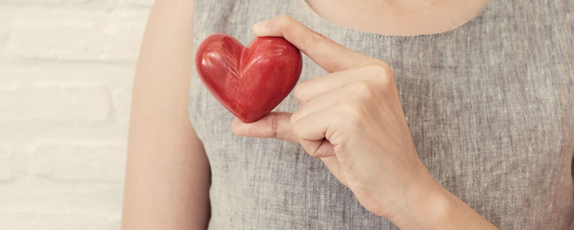 Allianz Gesundheitswelt - Herzgesundheit ritmo: Eine Frau mit Leinenoberteil hält ein rotes Holzherz in der Hand.