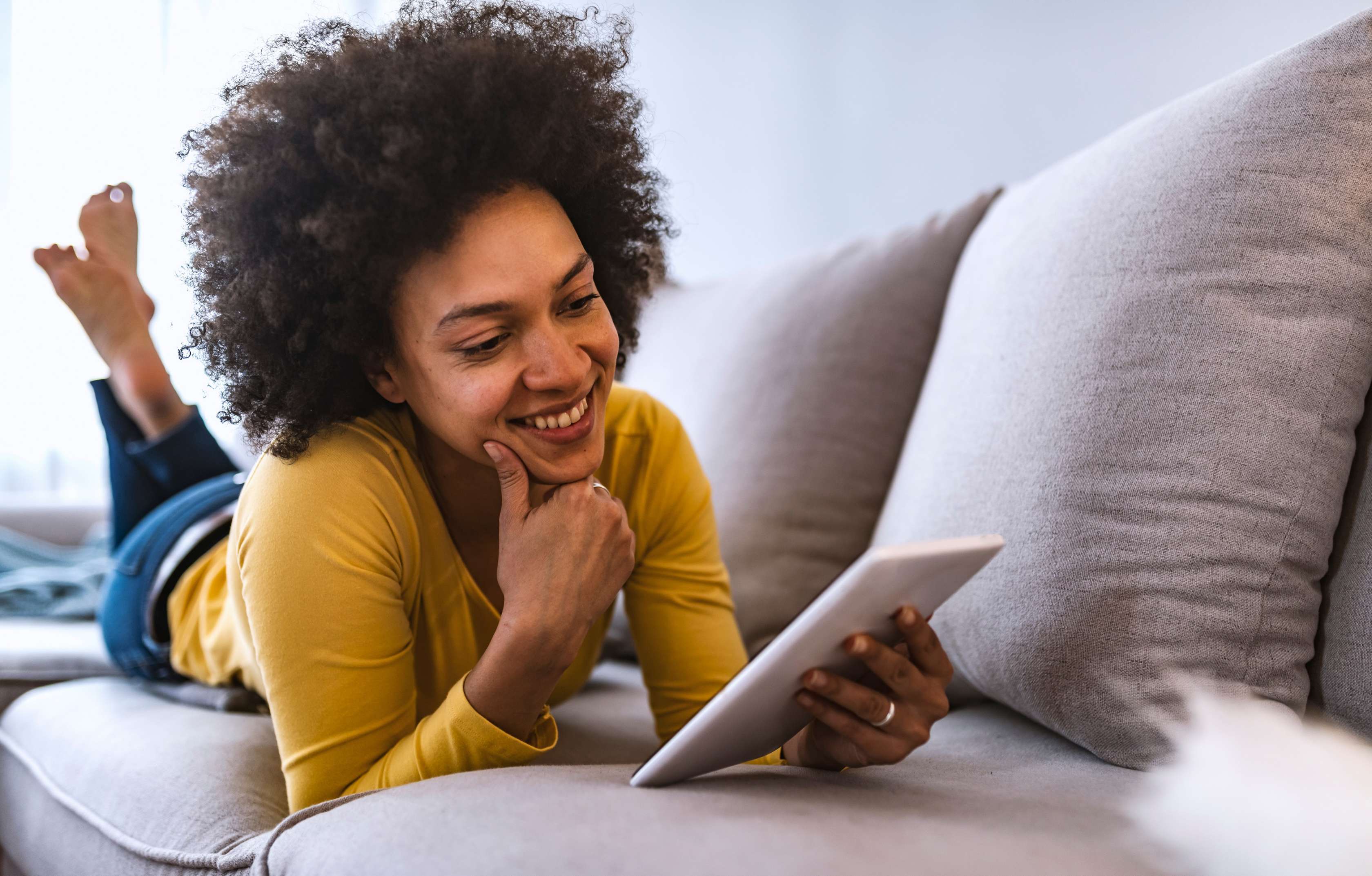 Allianz Gesundheitswelt - Infothek: eine junge Frau liegt auf der Couch und stöbert durch die Ratgeber der Allianz Infothek.