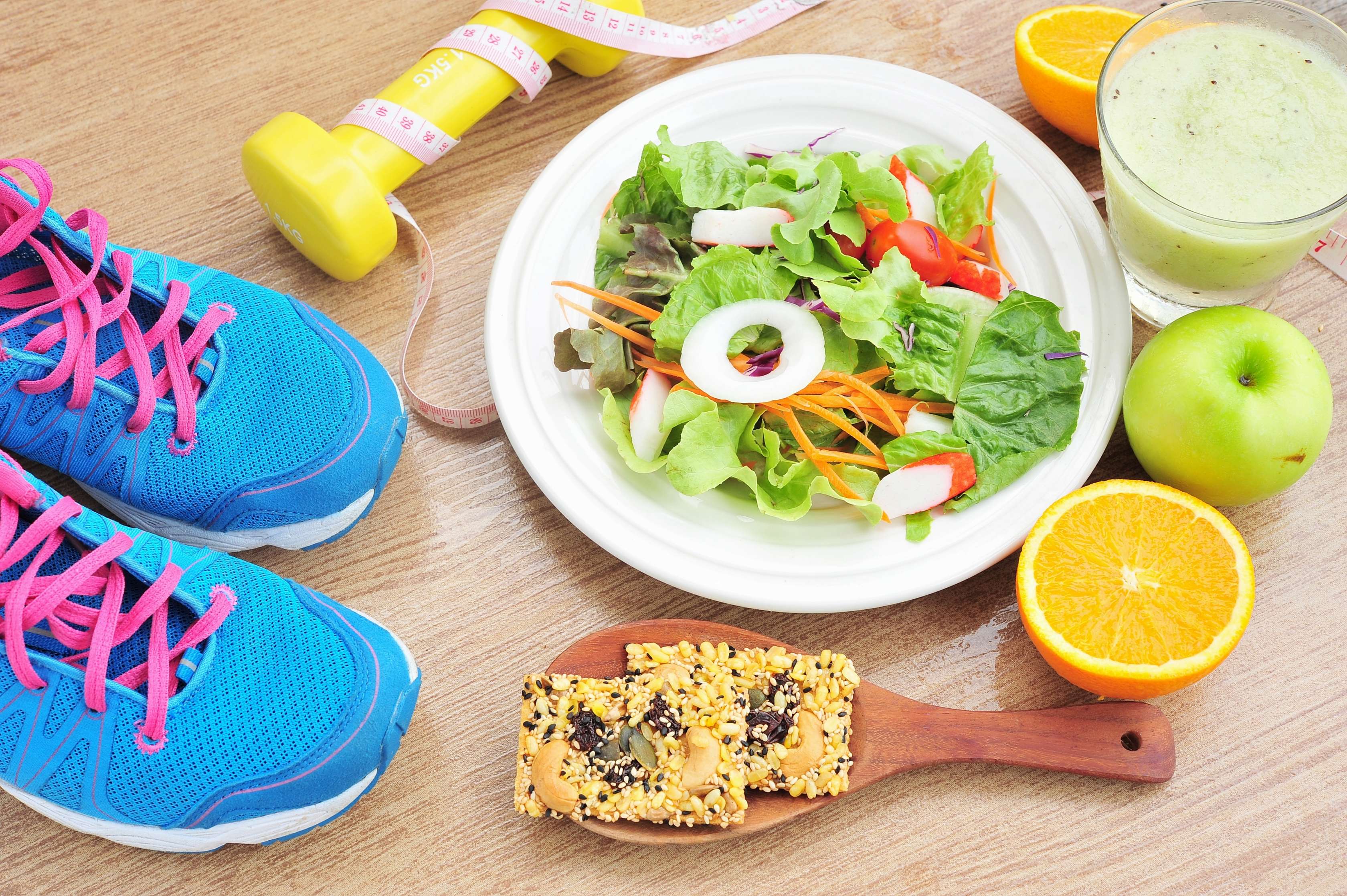 Allianz Gesundheitswelt - Mein GewichtsCoach: Ein Teller mit gemischtem Salat steht auf einem Holzuntergrund. Um den Teller sind gewichtsmanagende Lebensmittel und Sportgeräte zu sehen.