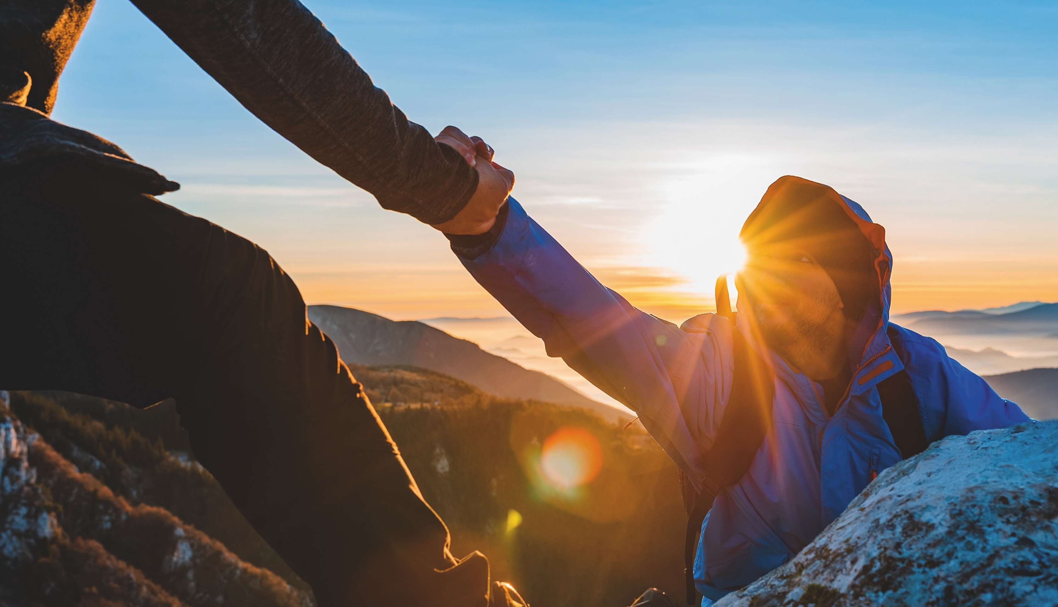 Allianz Gesundheitswelt - Parnernetzwer Psyche: zwei Bergsteiger erklimmen einen Gipfel. Ein Bersteiger hilf dem Anderen über einen Felsen.