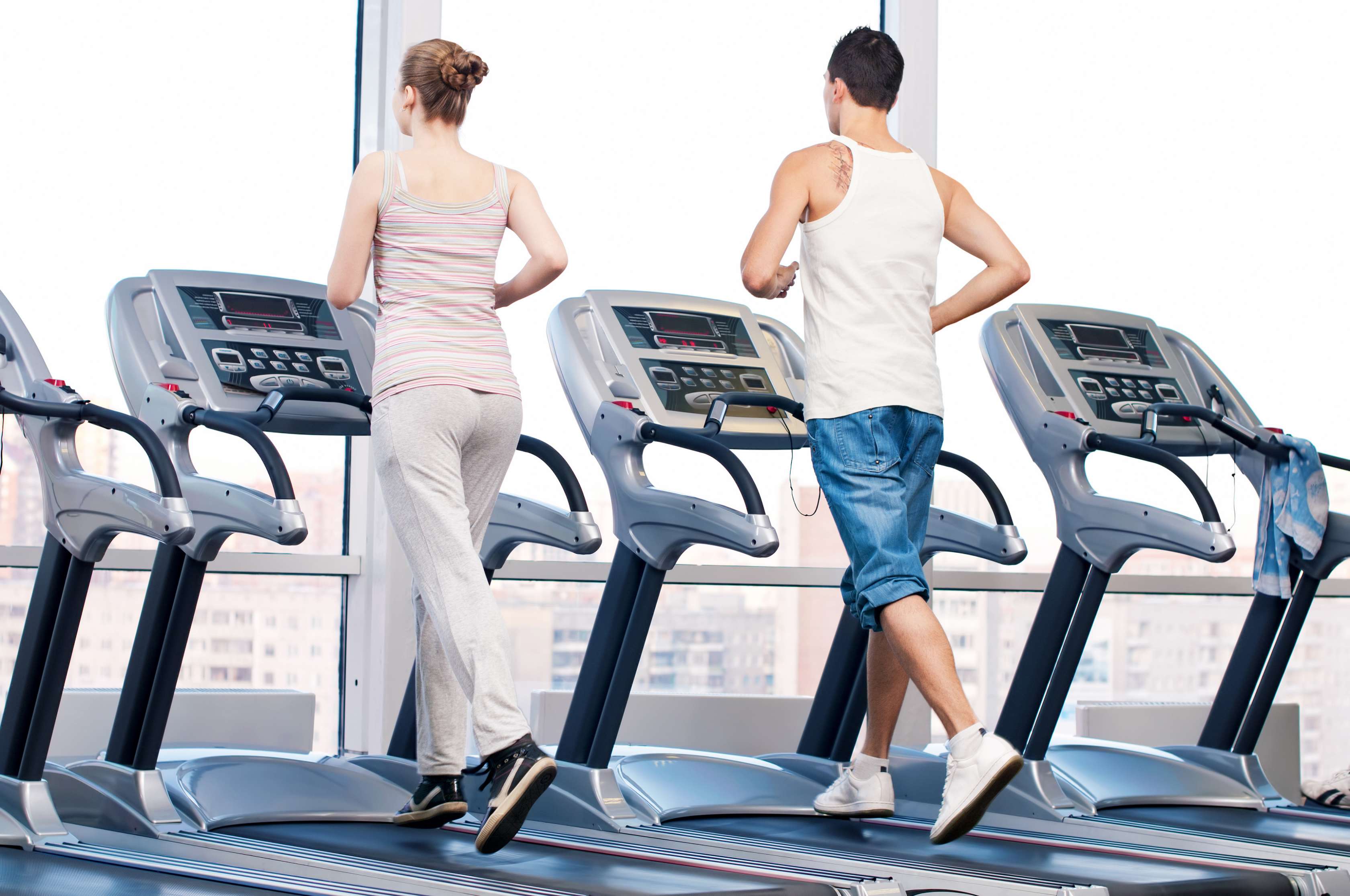 Allianz Gesundheitswelt - Fitnessstudio finden: Eine Frau mit geflochtenem Dutt und ein Mann mitz dunkelen Haaren laufen im Fitnessstudio auf Laufbändern.