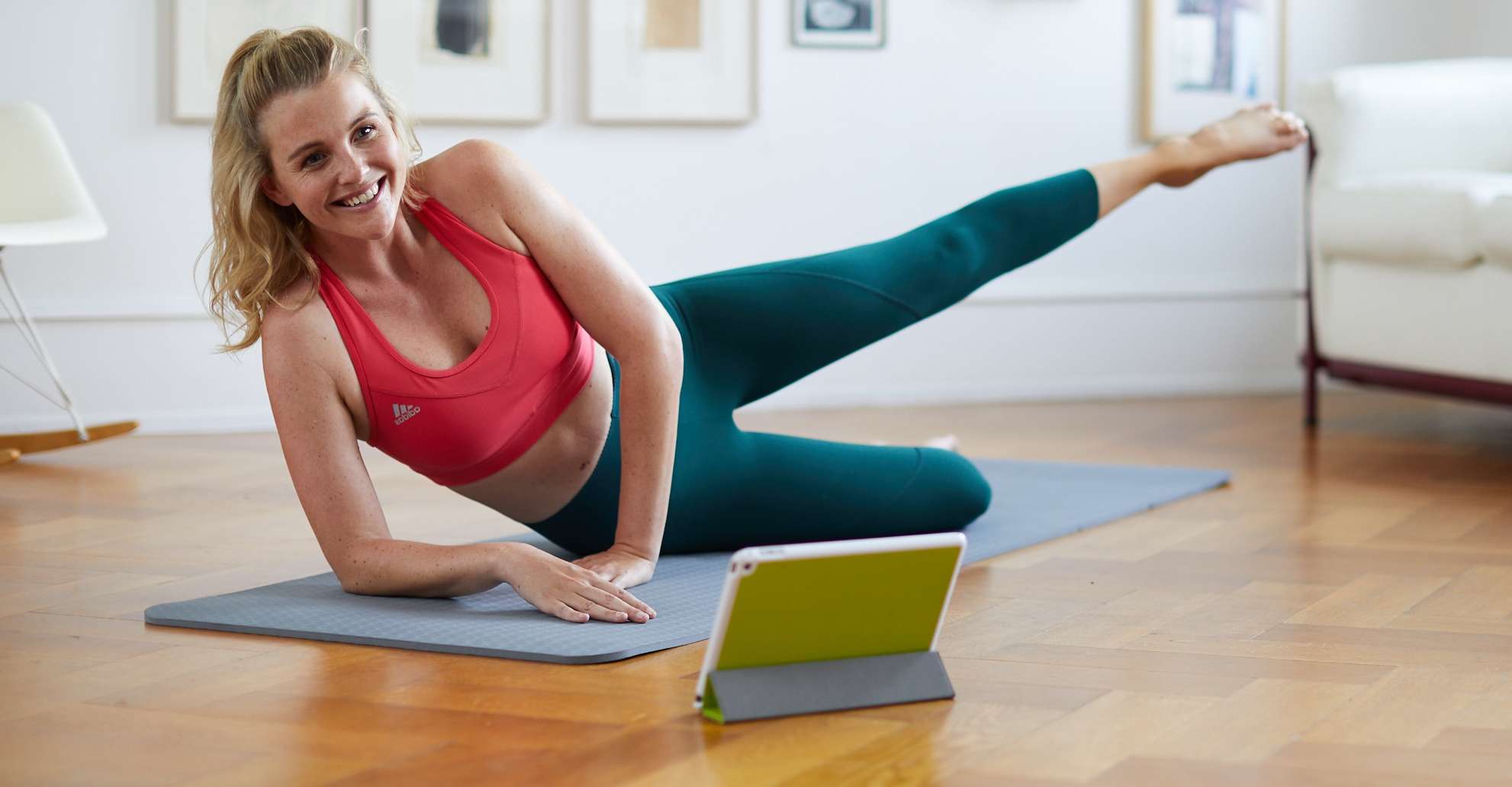 Allianz Gesundheitswelt - Mein Fitness Training: Eine junge Frau mit Pferdeschwanz und rotem Sport BH macht zuhause auf einer Sportmatte Fitnessübungen, die in der Mein Fitness-Trainingsapp der Allianz vorgeschlagen werden.