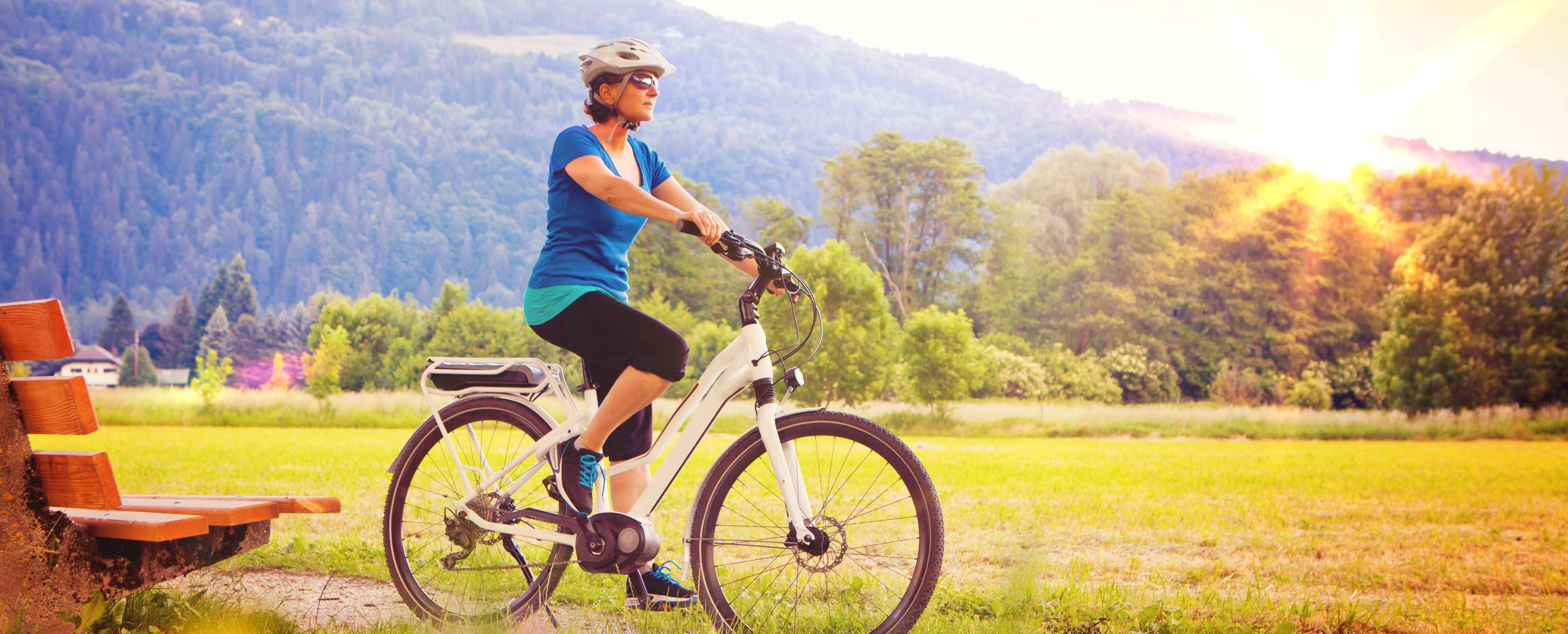 Allianz Gesundheitswelt - Pedelecs: eine Frai in Sportkleidung und mit Helm fährt mit einem Pedelec durch die Natur.
