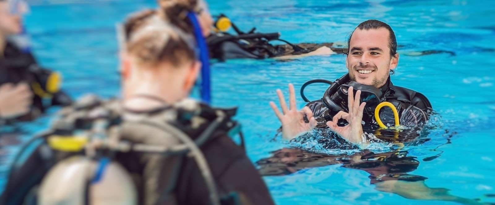 Allianz Gesundheitswelt - Tauchen lernen: Junger Mann mach tTauchzeichen in einem Schwimmbecken.